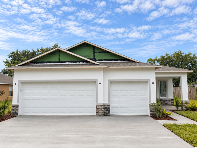 A partially completed house with a two-car garage, featuring a stone facade and a clear blue sky.