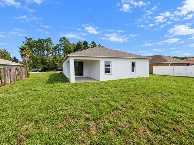 A backyard view of a single-story home with a grassy lawn and blue sky.