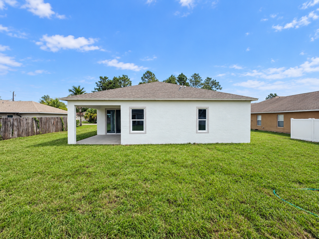 A single-story white house with a porch and large grassy backyard under a blue sky.