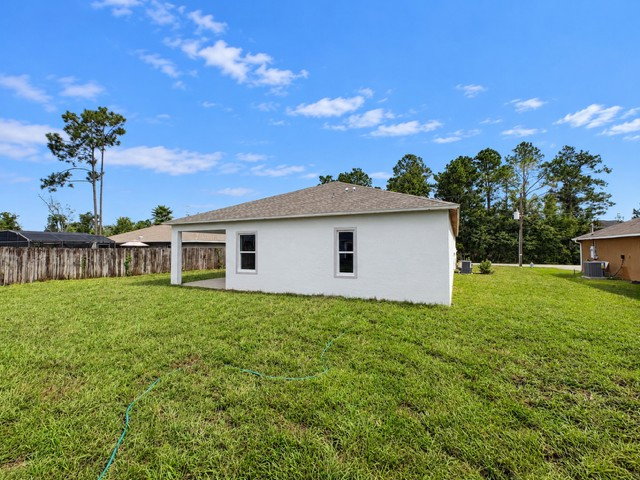 A white house with a porch and large green yard under a blue sky with scattered clouds.