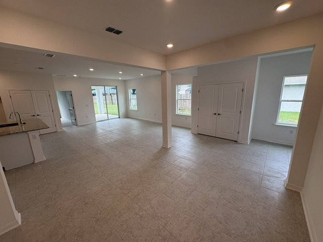 Spacious, well-lit living area with tile flooring and large windows, leading to a backyard.