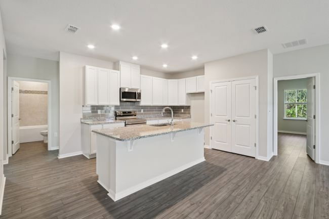 Modern kitchen featuring white cabinetry, a granite island, stainless steel appliances, and an open layout.