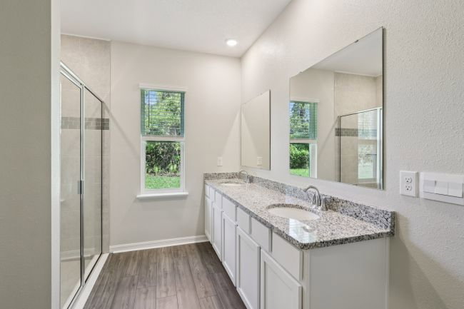 Modern bathroom featuring a double vanity with a granite countertop, a large mirror, a walk-in shower, and natural light from a window.