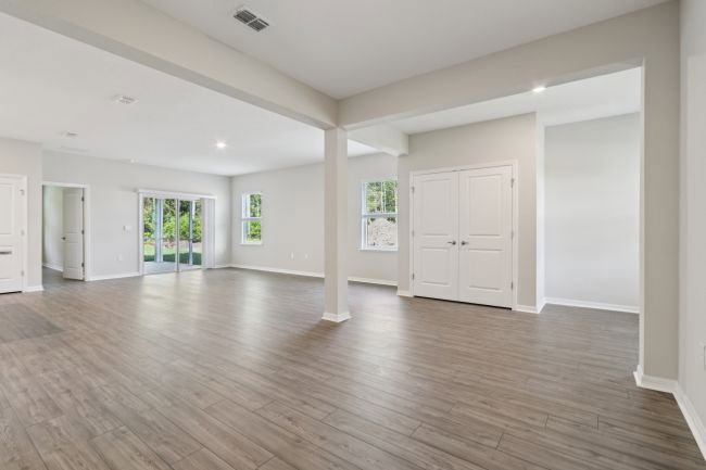 Spacious, empty living room with large windows and wood-like flooring.