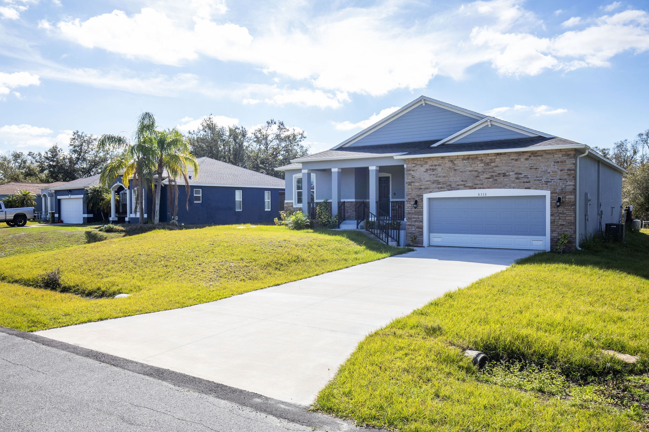 A modern suburban house with a stone facade, well-kept lawn, and attached garage under a clear blue sky.