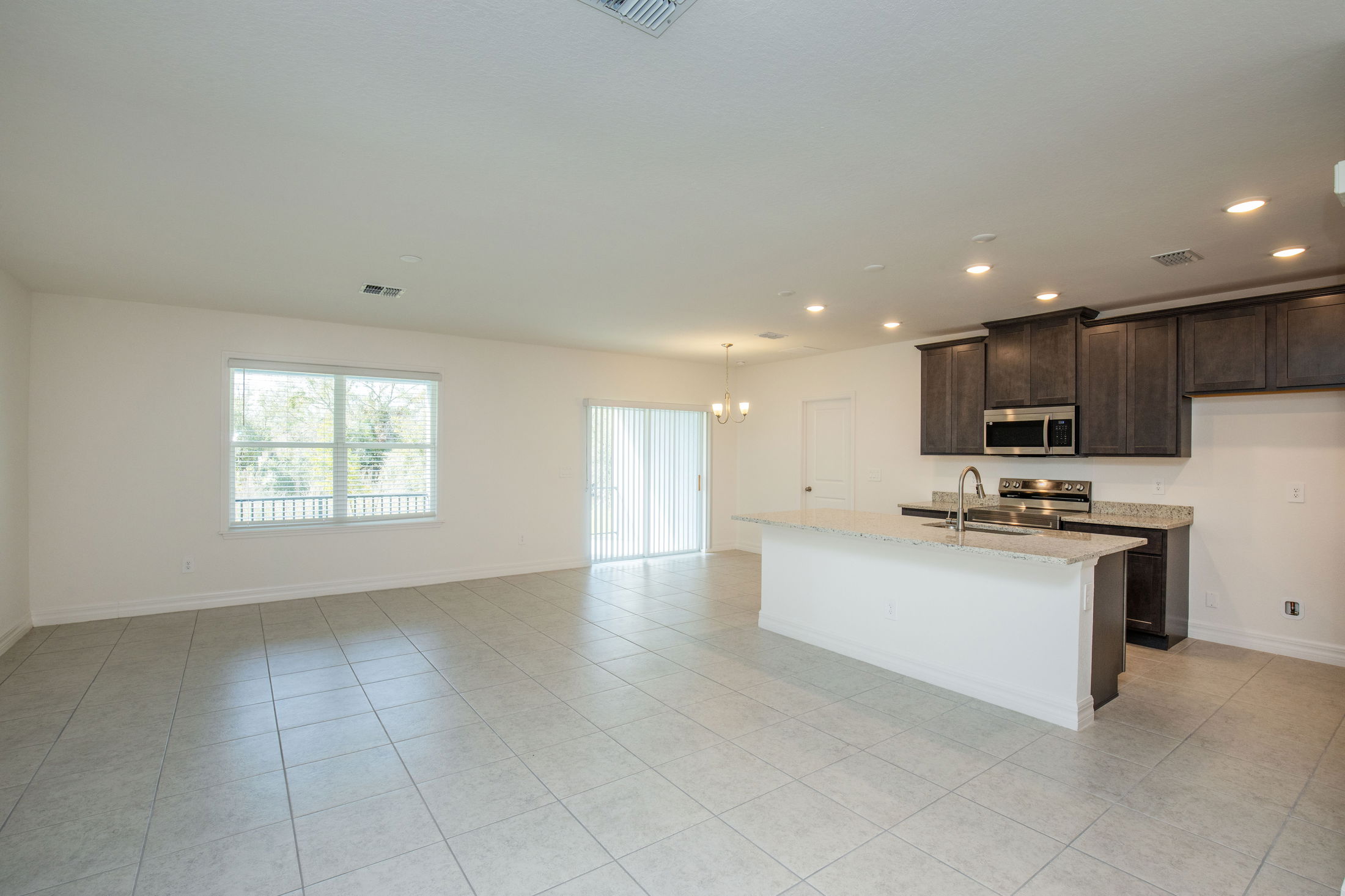 Modern open-concept kitchen and living area with large windows, tiled flooring, and dark wood cabinets.