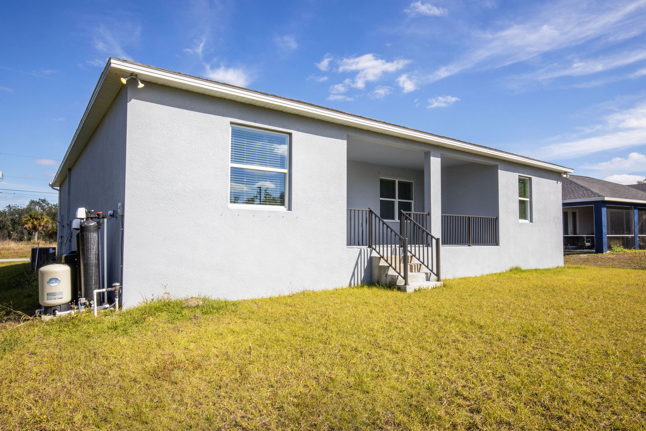 A modern one-story home with a gray stucco exterior, small porch, and neatly trimmed lawn under a clear blue sky.