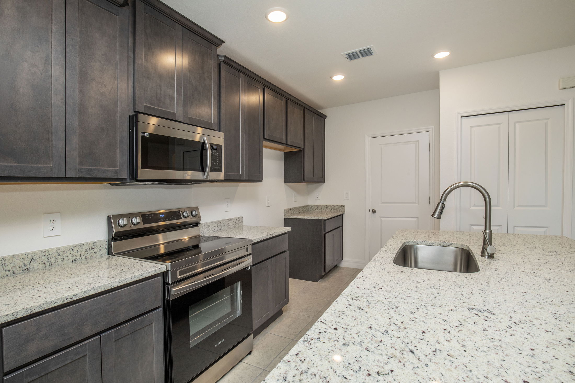 Modern kitchen with dark wood cabinets, stainless steel appliances, and granite countertops featuring a sink island.