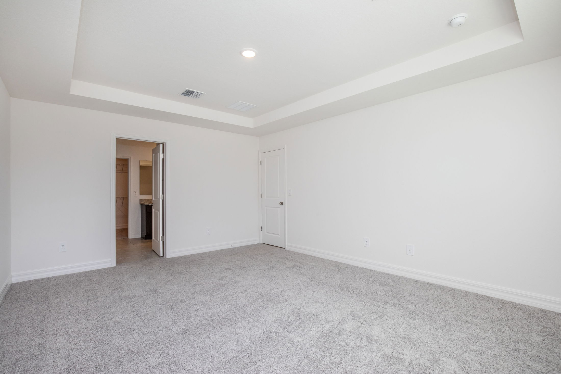 Spacious empty room with white walls, recessed ceiling, and carpet flooring featuring two doors.