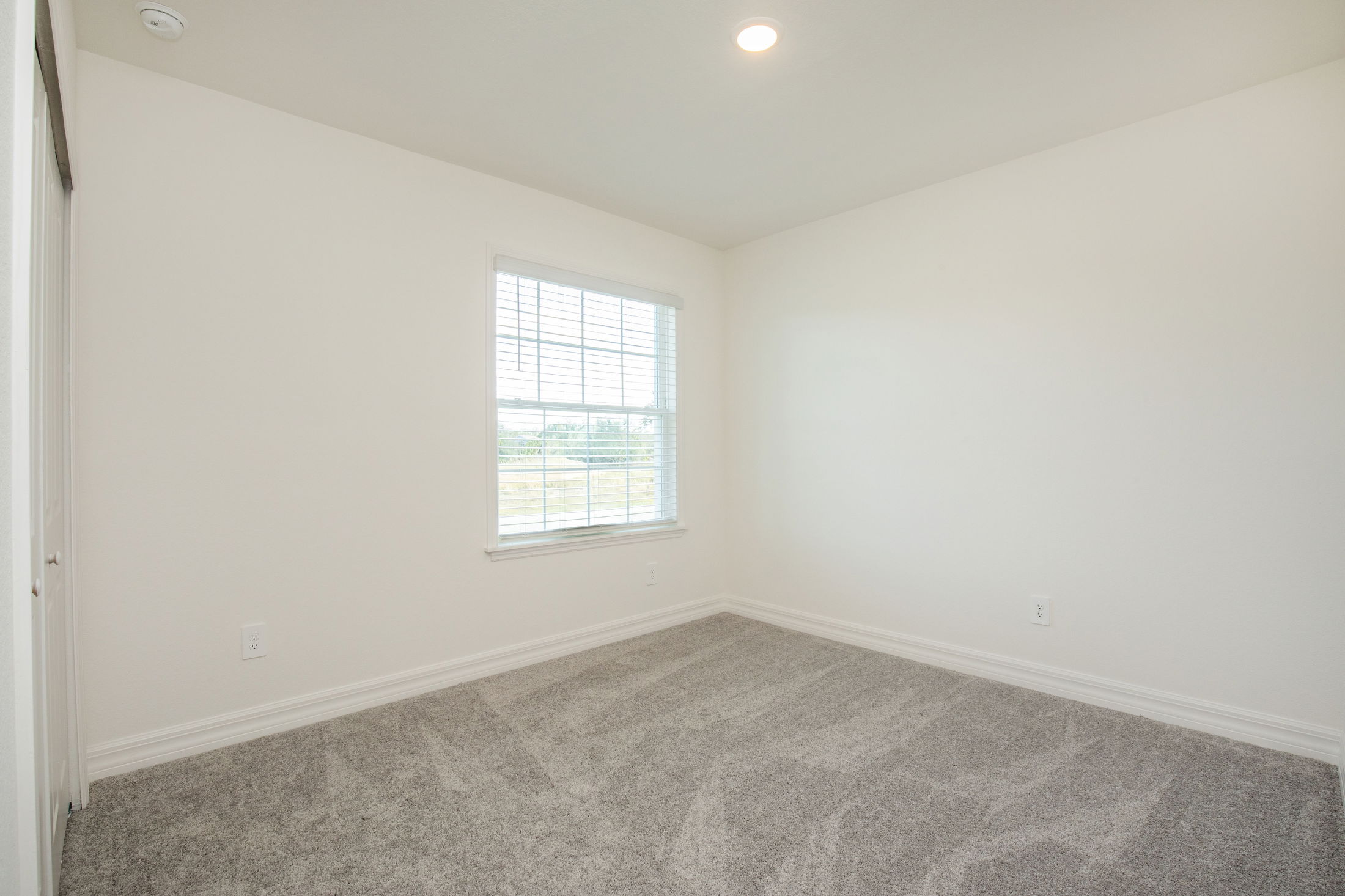 Empty room with white walls, grey carpet, and a window letting in natural light.