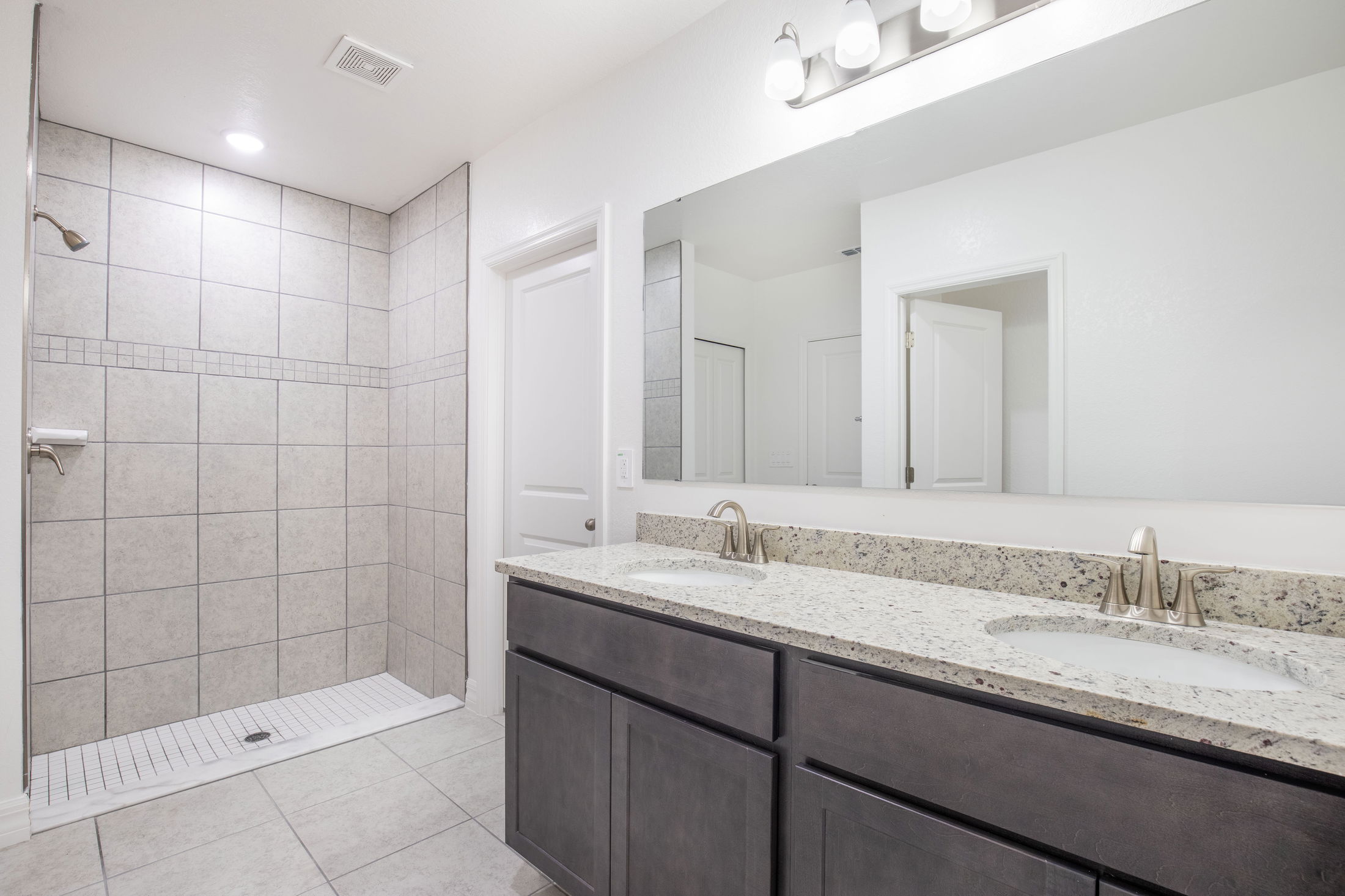 Modern bathroom with a walk-in tiled shower and double-sink vanity with granite countertop.