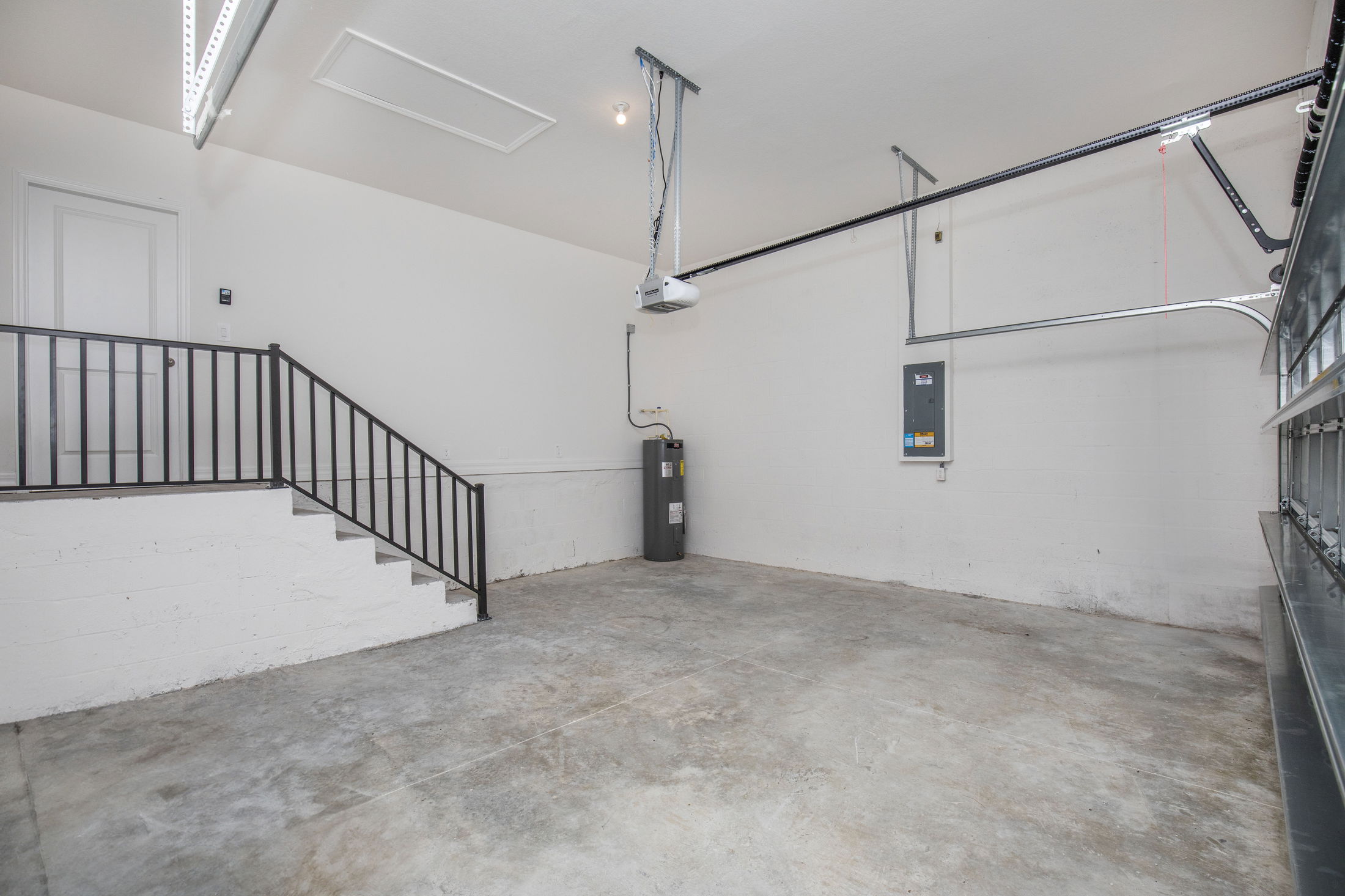 Spacious, clean residential garage with concrete floor, water heater, overhead door opener, and staircase access.