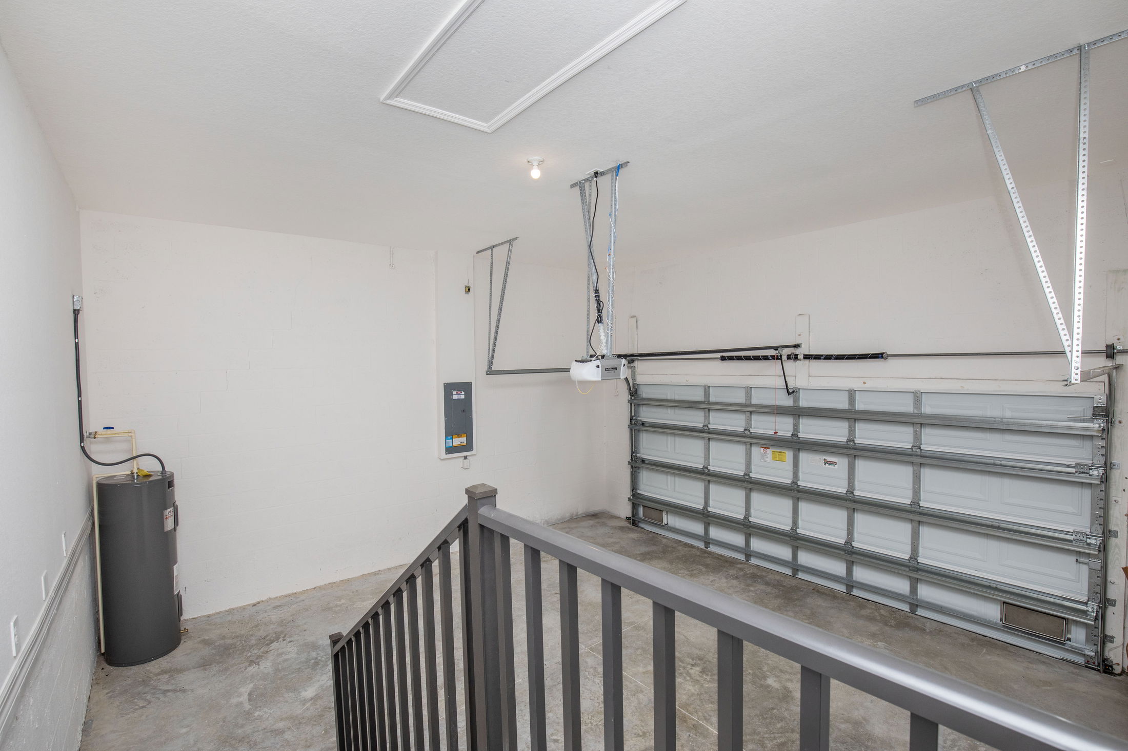 Empty residential garage with metal garage door, water heater, and electrical panel.