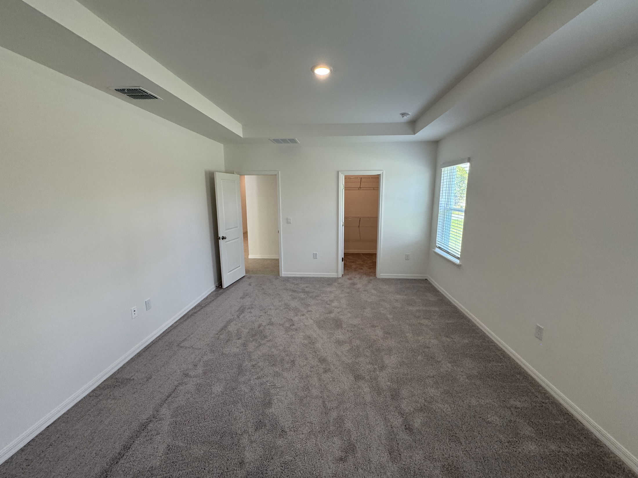 Empty carpeted room with white walls, a ceiling light, and an open door leading to a closet.