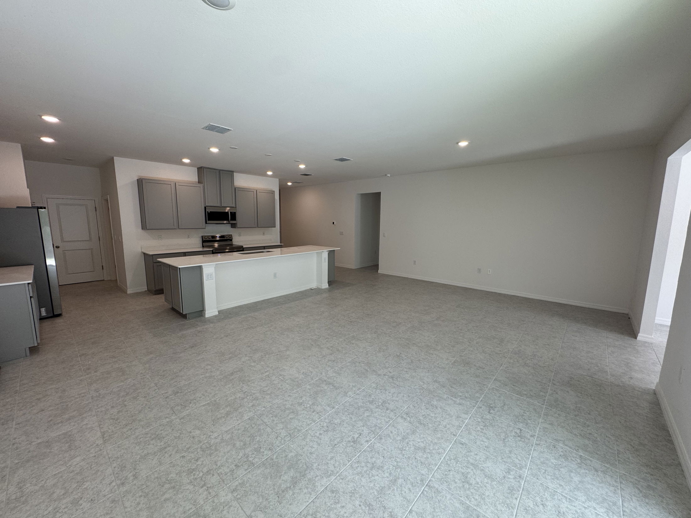 Spacious modern kitchen and living area with gray cabinetry and tile flooring in a new home.