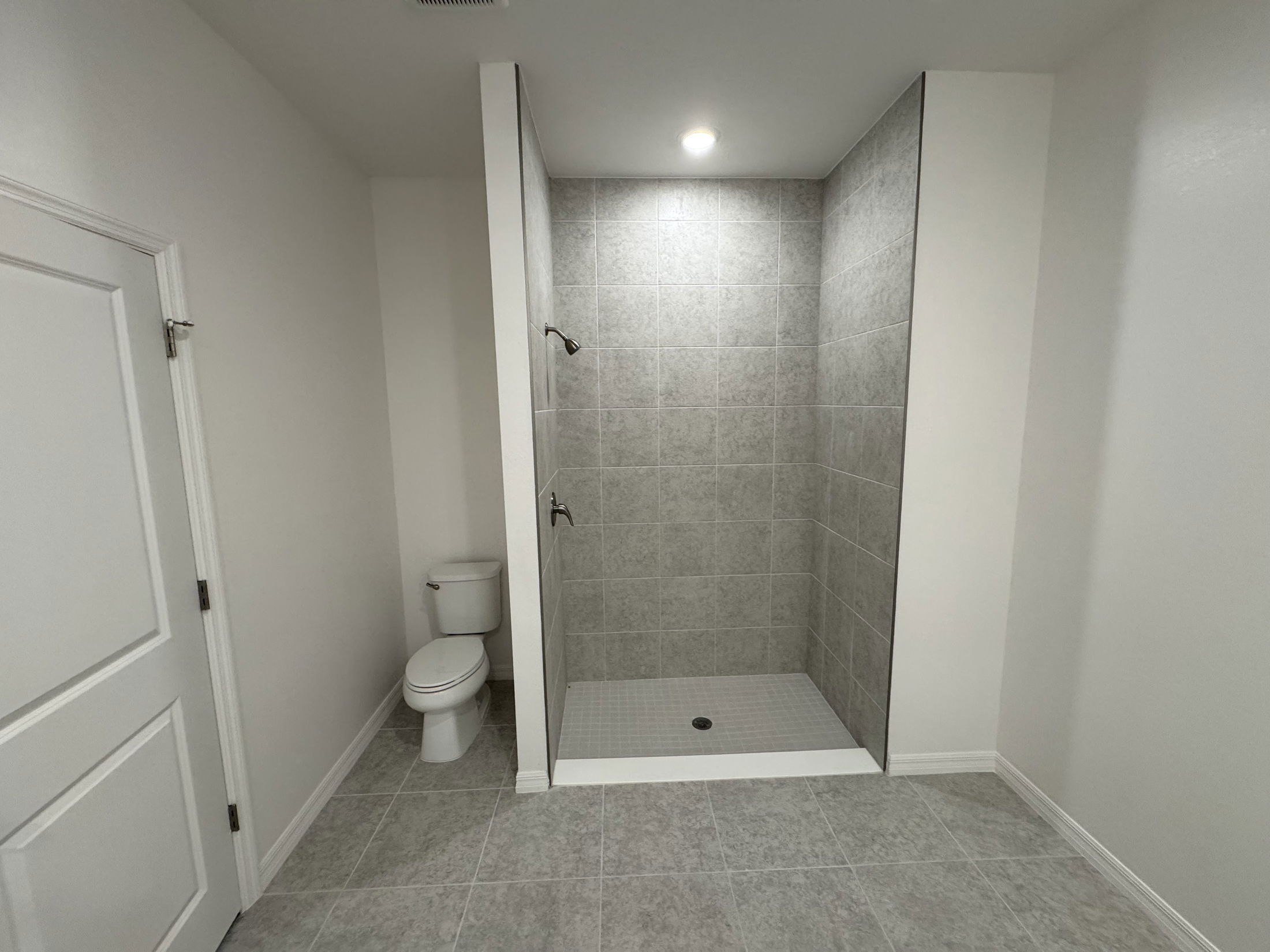 Minimalist bathroom featuring a walk-in shower with gray tiles and a toilet on a tiled floor.