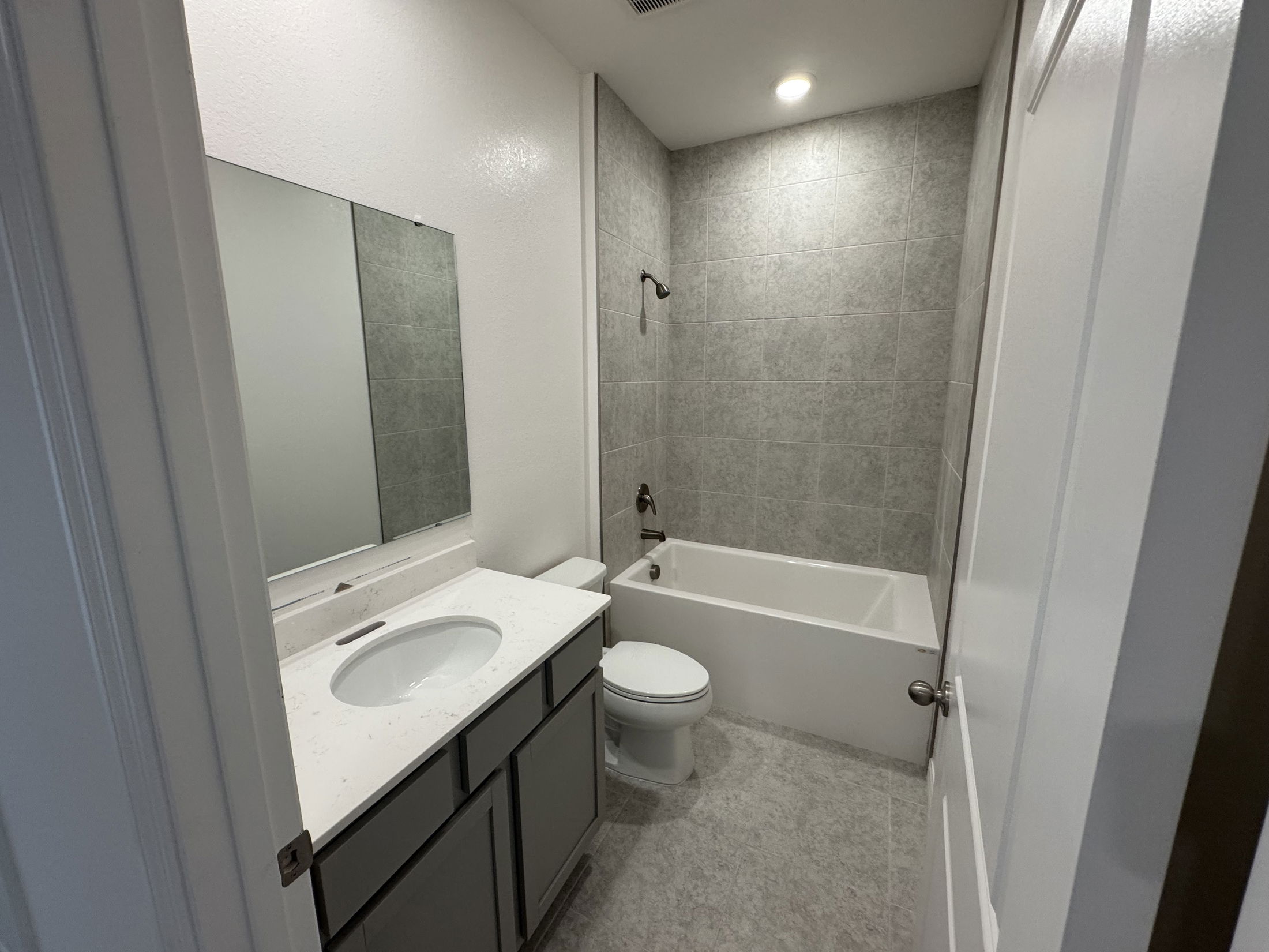 Modern bathroom with a gray tiled shower, white bathtub, and sleek vanity featuring a marble countertop.