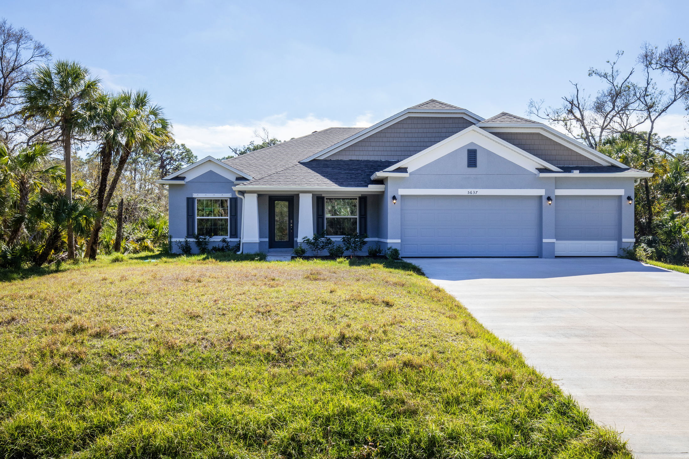 Modern single-story home with a two-car garage, surrounded by lush greenery and palm trees.