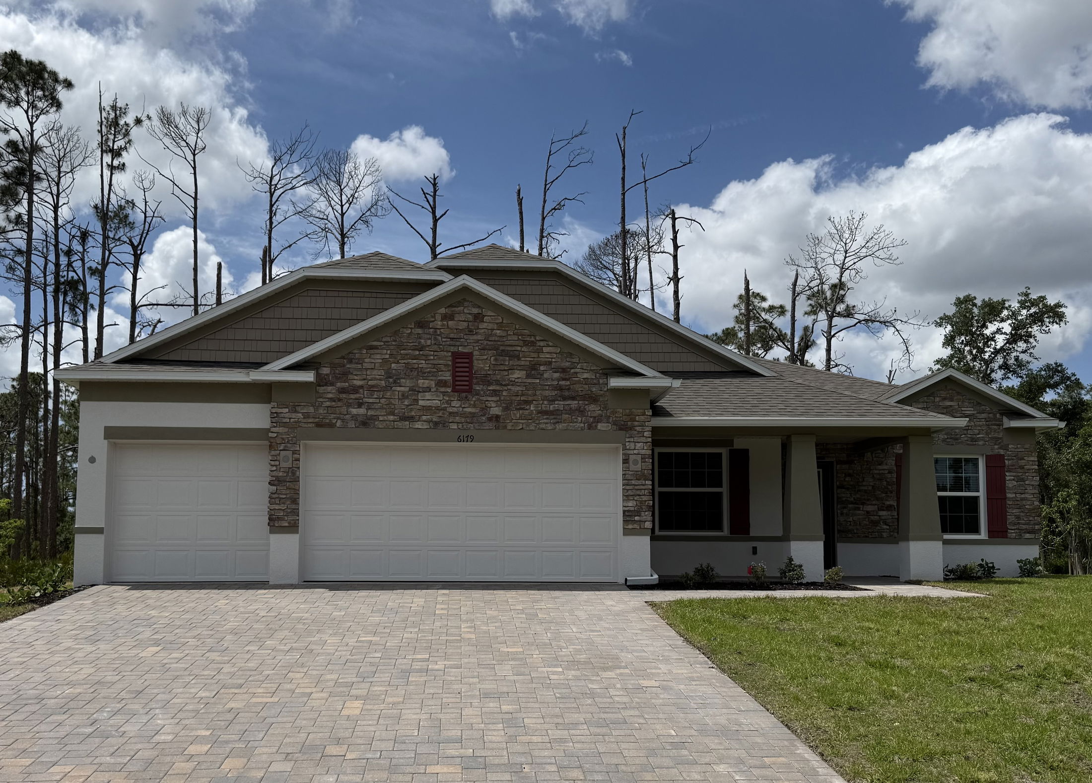 Modern suburban home with stone facade and three-car garage under a blue sky.