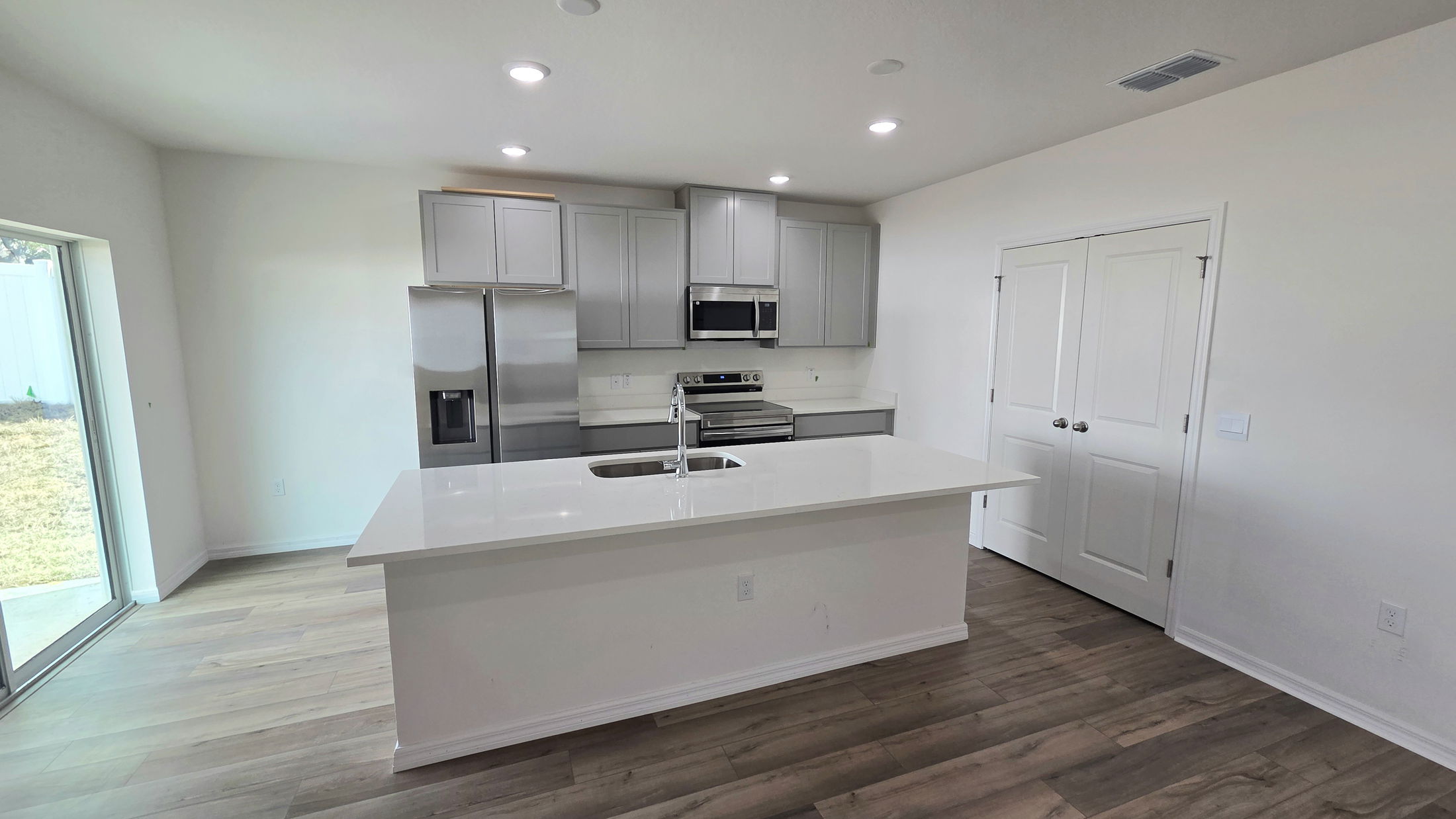 Modern kitchen interior featuring stainless steel appliances, gray cabinetry, and a large island with a white countertop.