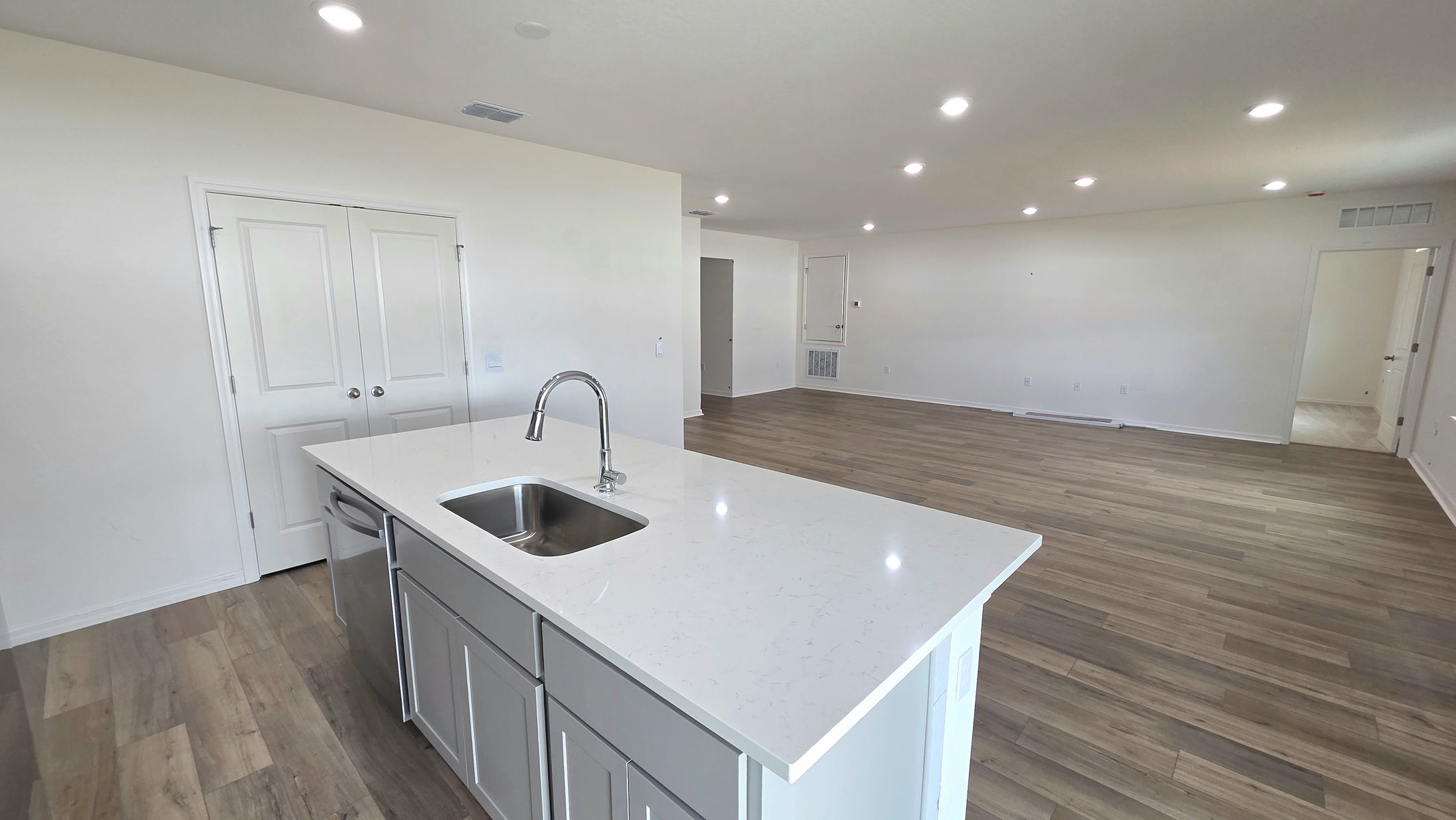 Modern kitchen with white quartz countertop, stainless steel sink, and open floor plan leading to a spacious living area.