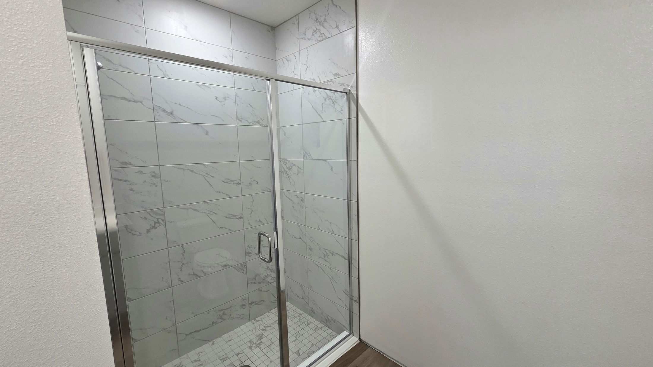 Modern shower with glass enclosure featuring sleek marble tile design and light wood flooring.