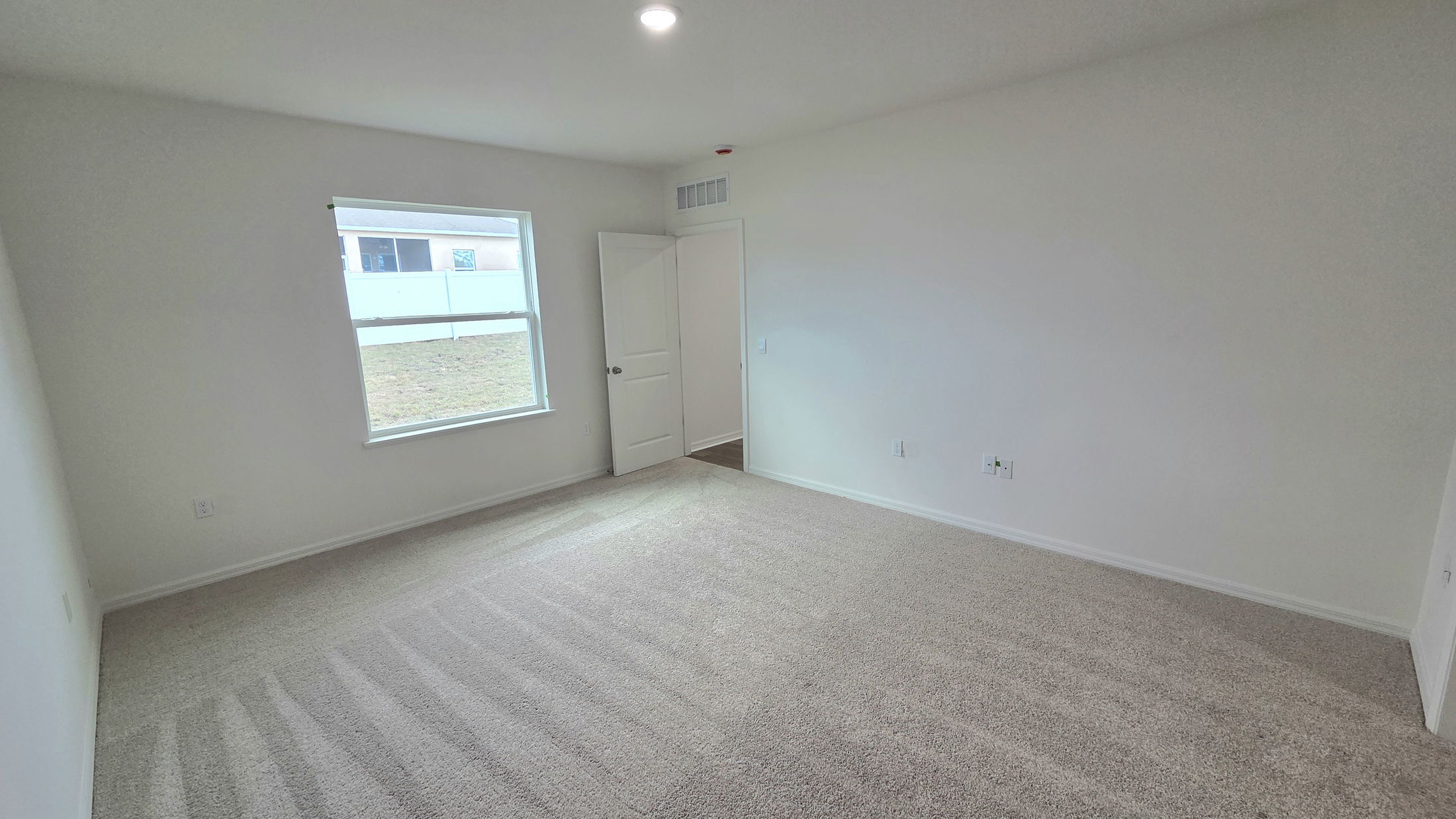 Spacious, empty room with beige carpet and a large window, ideal for a bedroom or home office.