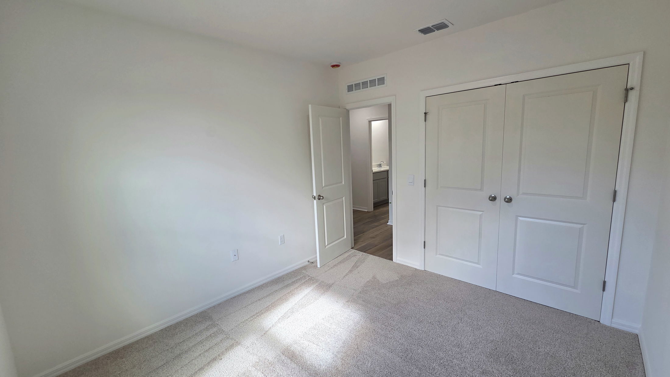 Spacious empty bedroom with neutral-colored walls, carpet flooring, and two closet doors.
