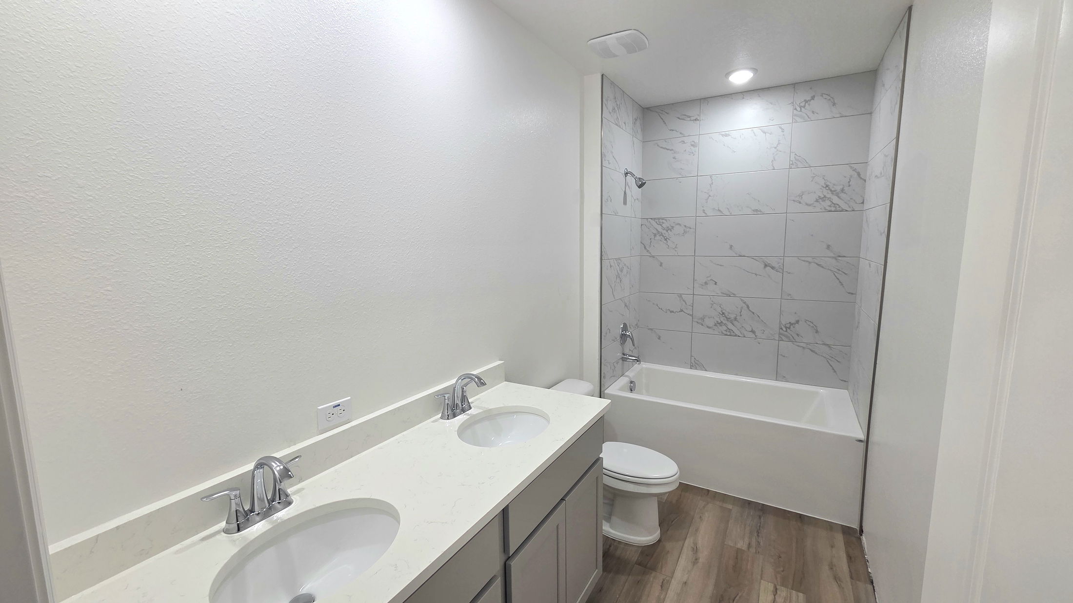 Modern bathroom featuring double sinks, marble-patterned tiles, and a bathtub with wood-like flooring.