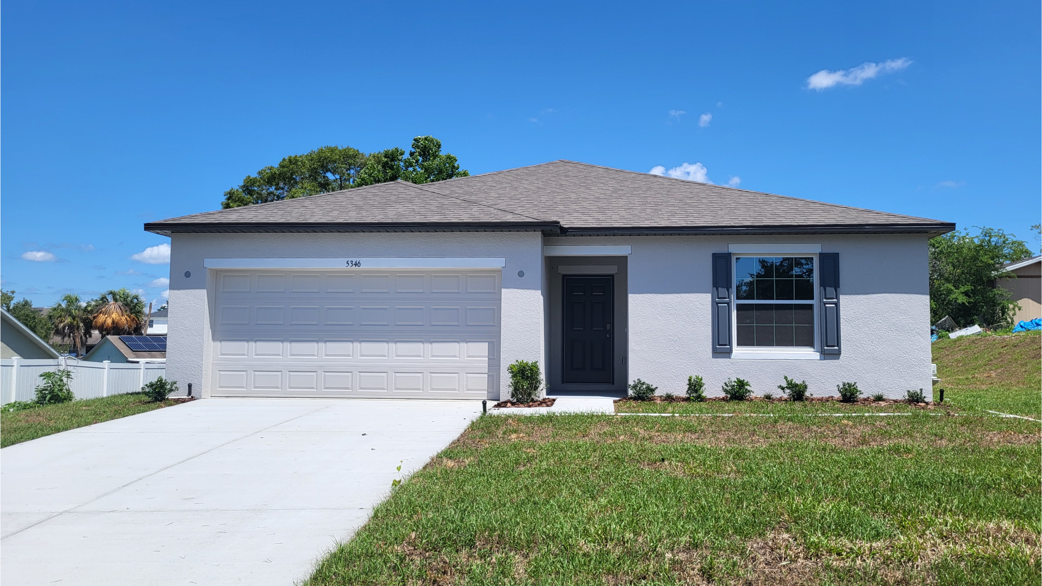 A modern single-story home with a two-car garage, gray roof, and manicured lawn under a clear blue sky.