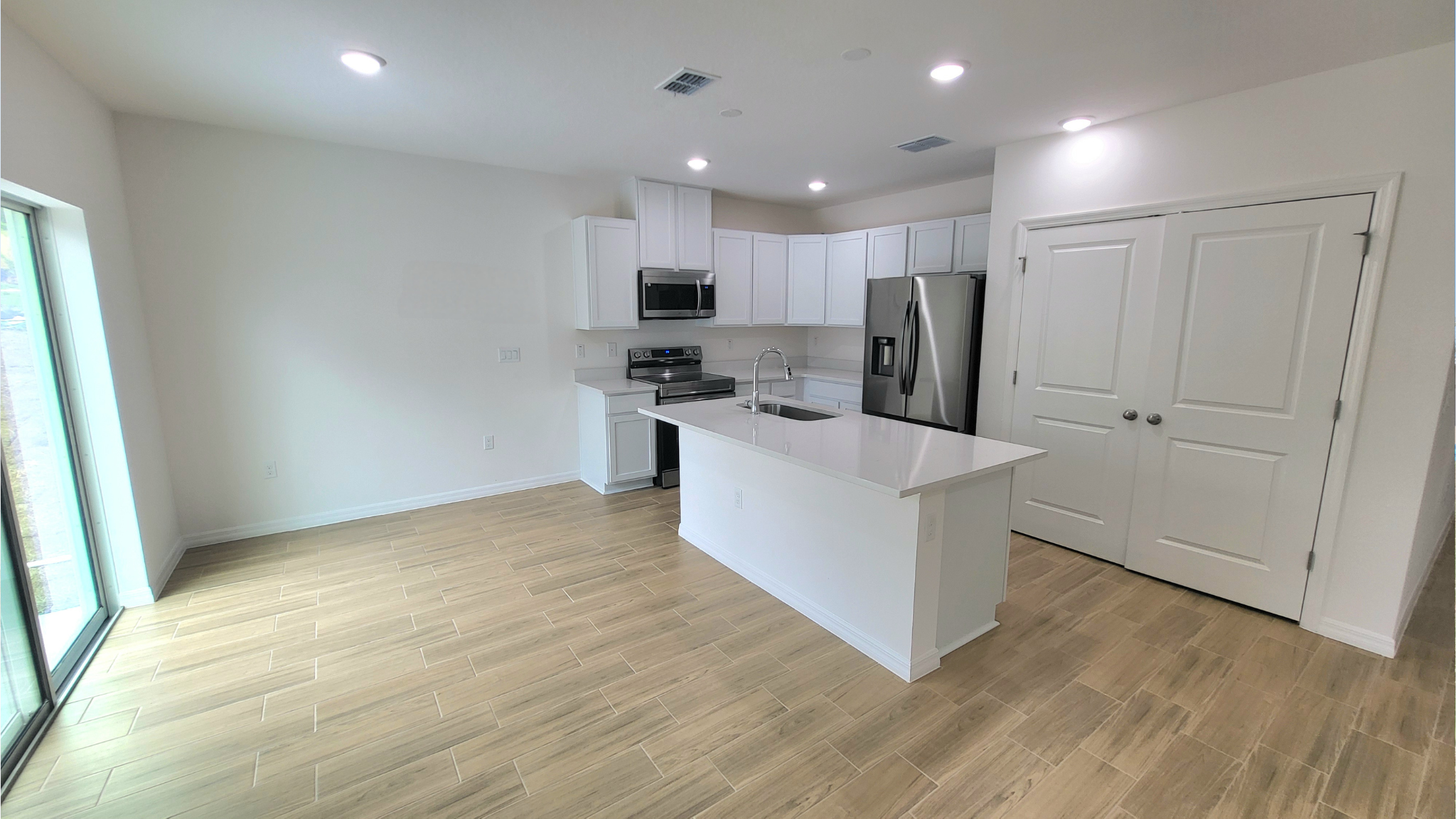Modern kitchen with white cabinetry, stainless steel appliances, and wooden flooring in a bright, open floor plan layout.