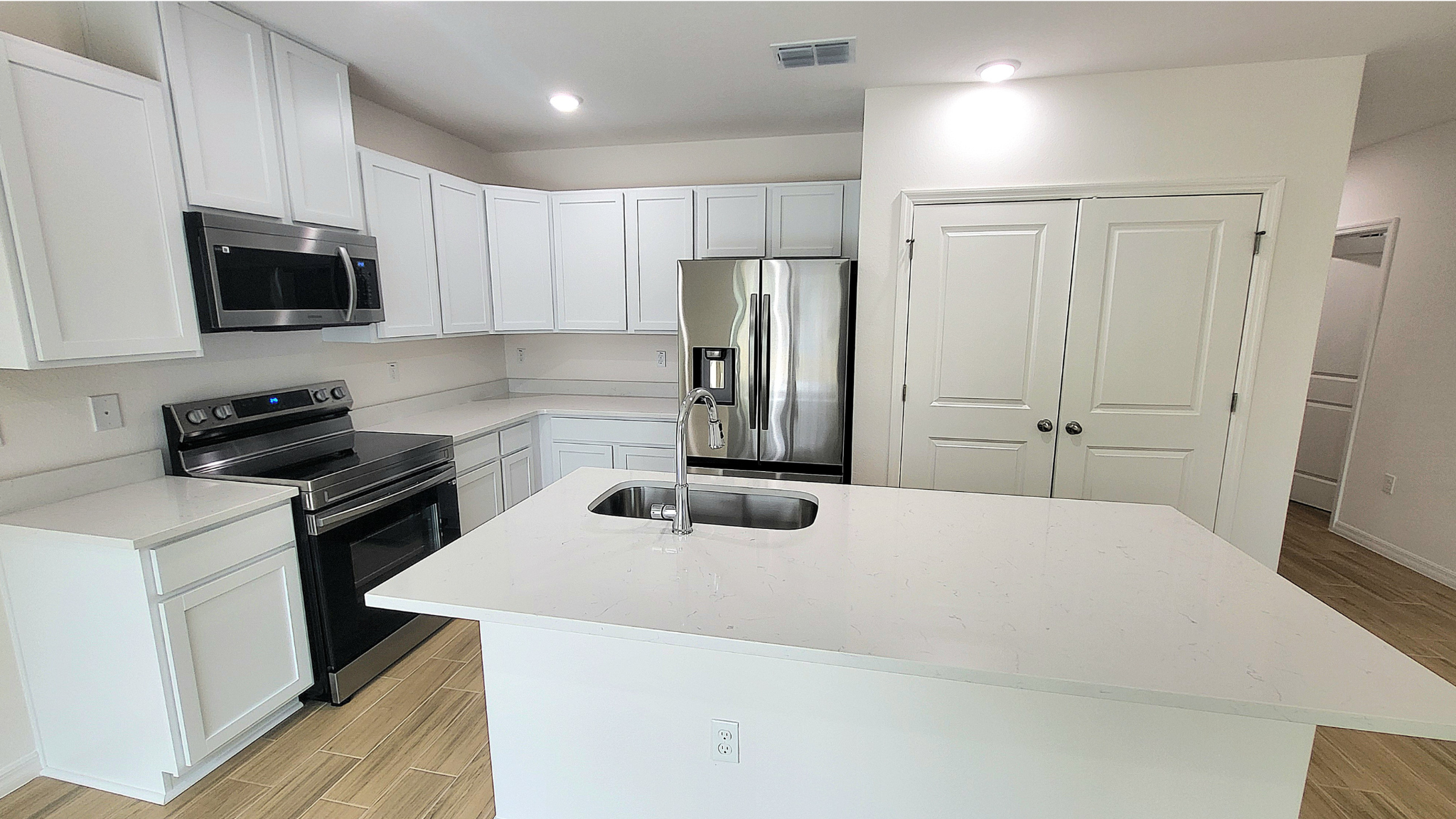 Modern kitchen with white cabinetry, stainless steel appliances, and a central island sink.