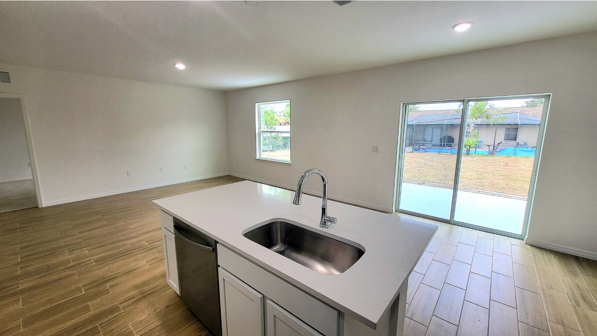 Modern kitchen with island and stainless steel sink overlooking a bright living area with sliding glass doors to the backyard.