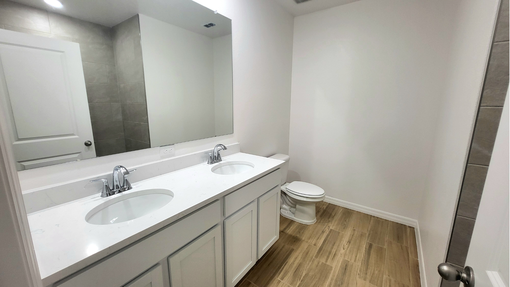 Modern bathroom with double vanity, marble countertop, large mirror, and wooden floors.