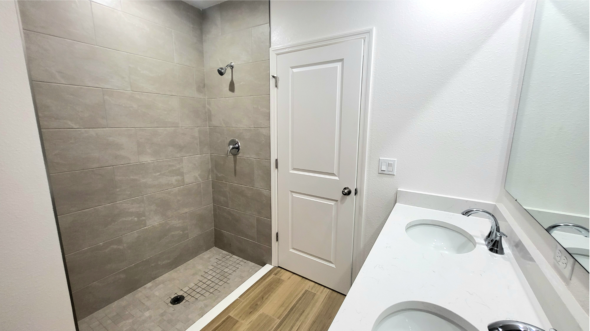 Modern bathroom with tiled walk-in shower, dual-sink vanity, and wooden floor accents.