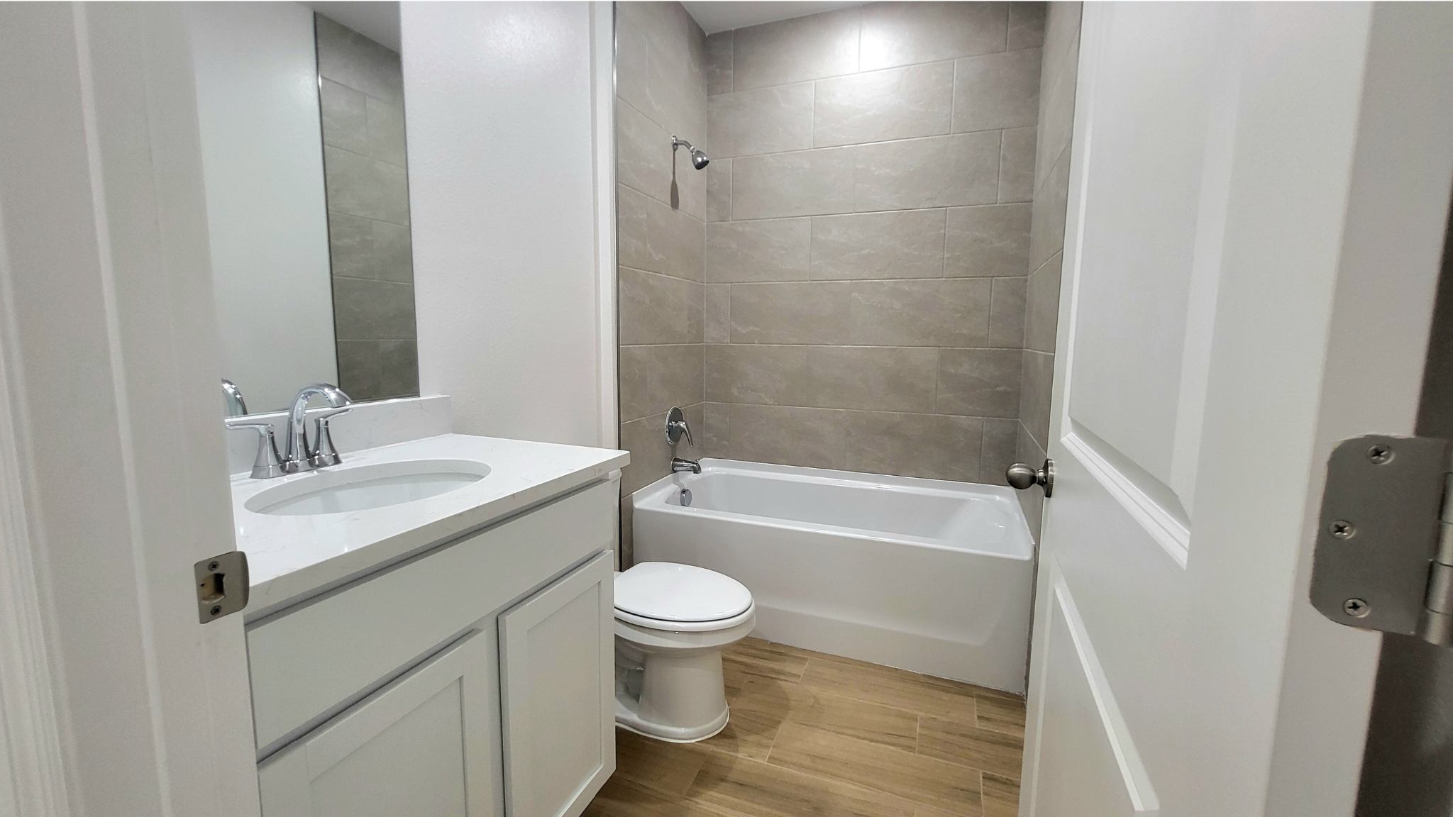 Modern bathroom with a white vanity, oval sink, and bathtub with tiled walls and wooden flooring.