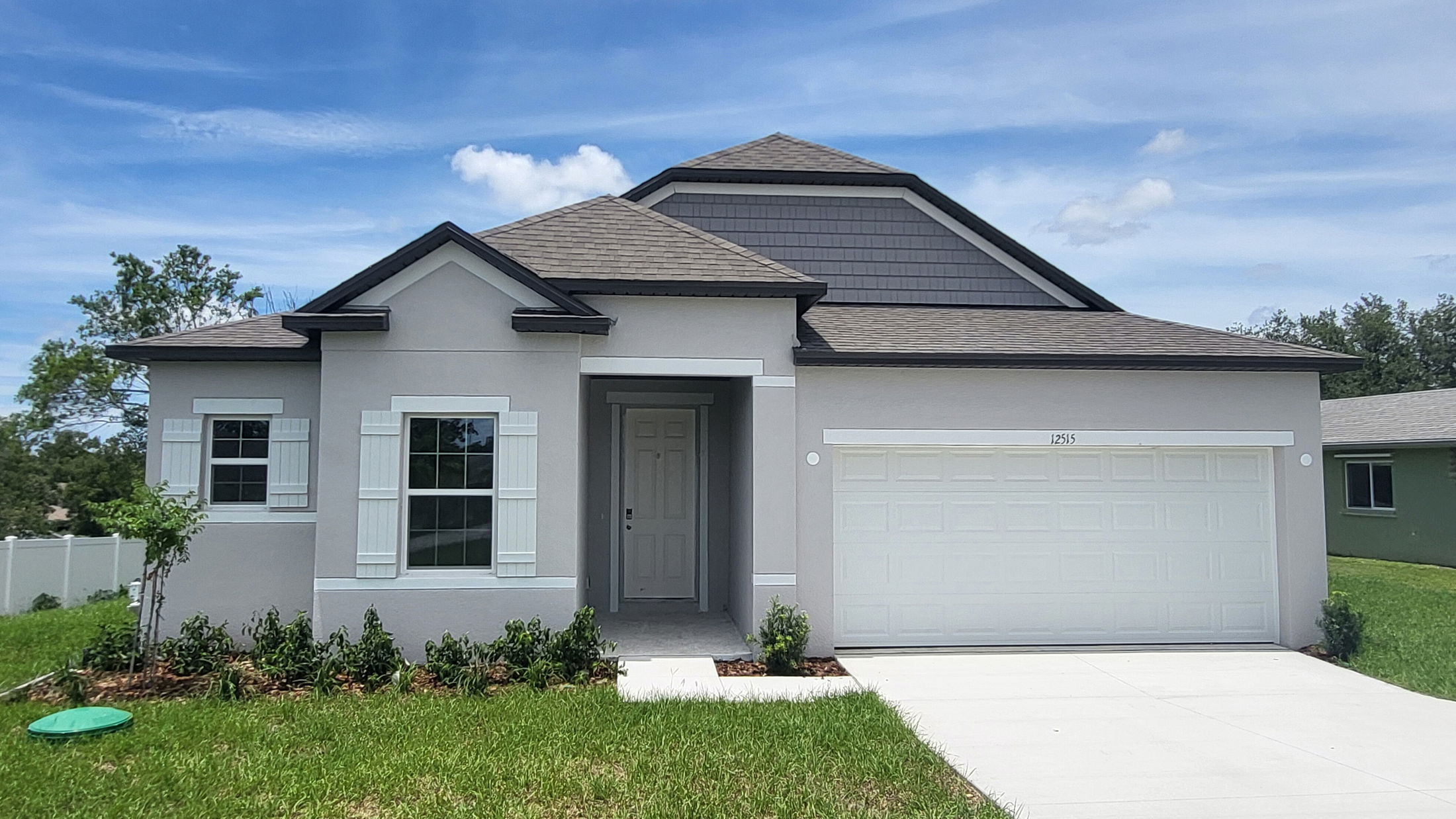 Modern single-story gray house with manicured lawn, white garage door, and blue sky background.