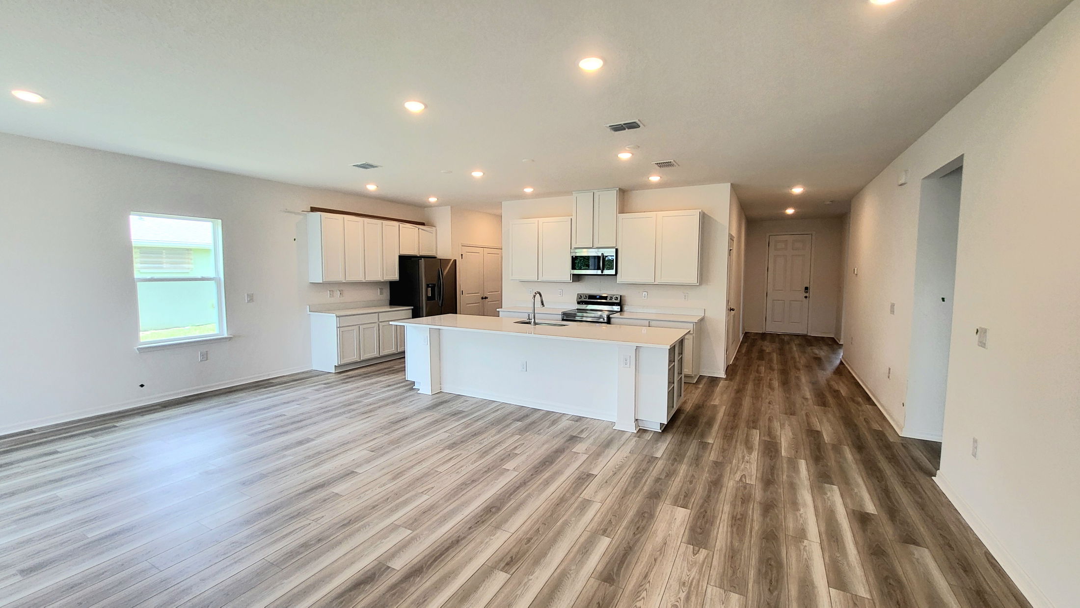 Modern kitchen with white cabinetry and island, stainless steel appliances, and wood-style flooring in an open-concept layout.