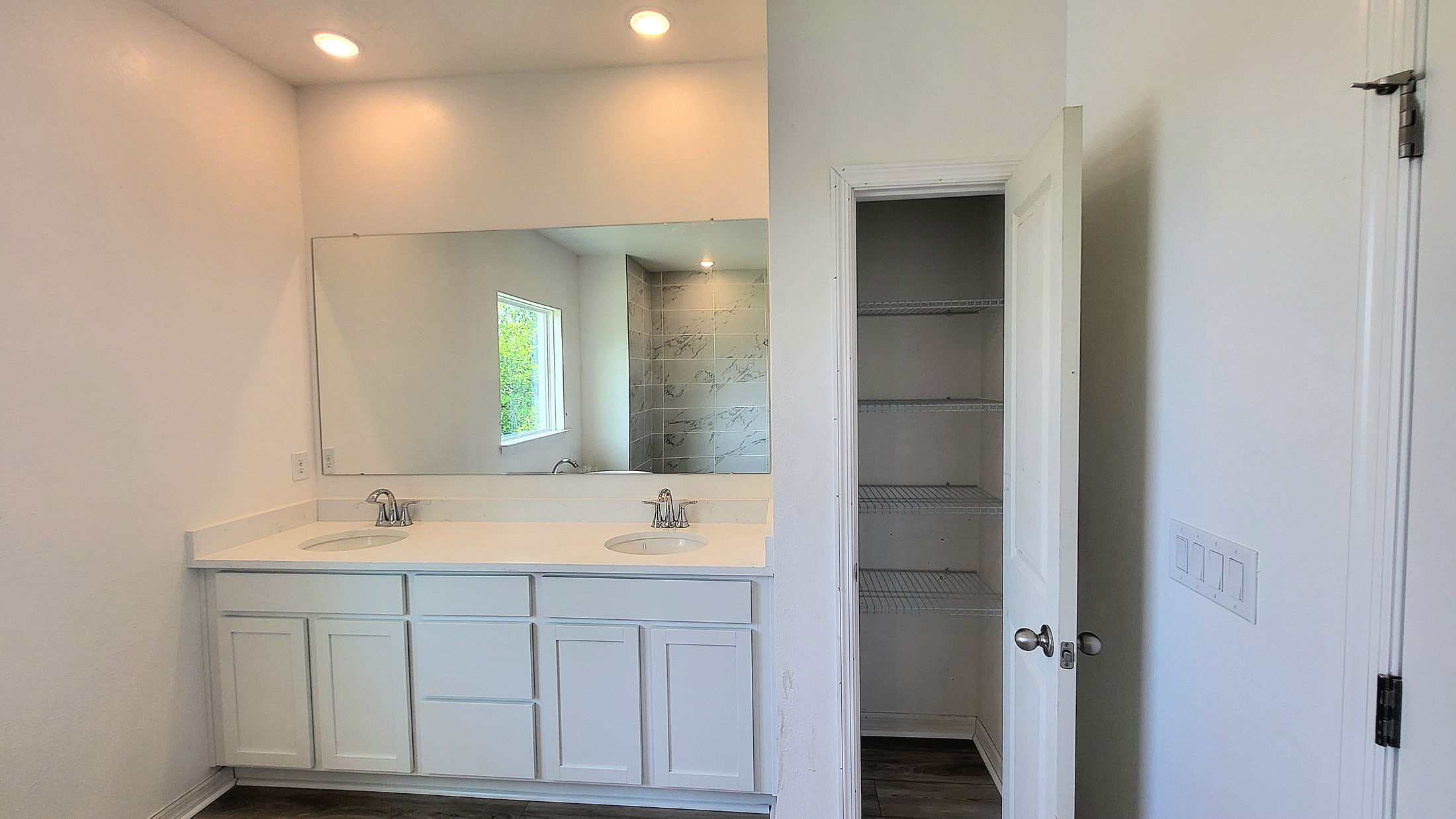 Modern bathroom with a double sink vanity, large mirror, and open closet with white shelving.