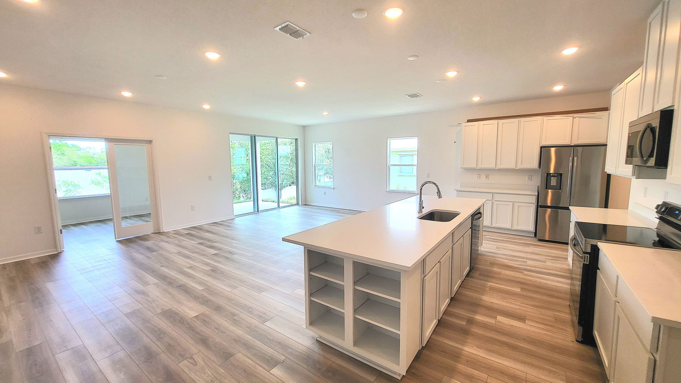 Modern, open-concept kitchen and living area featuring a large island, stainless steel appliances, and wood-look flooring.