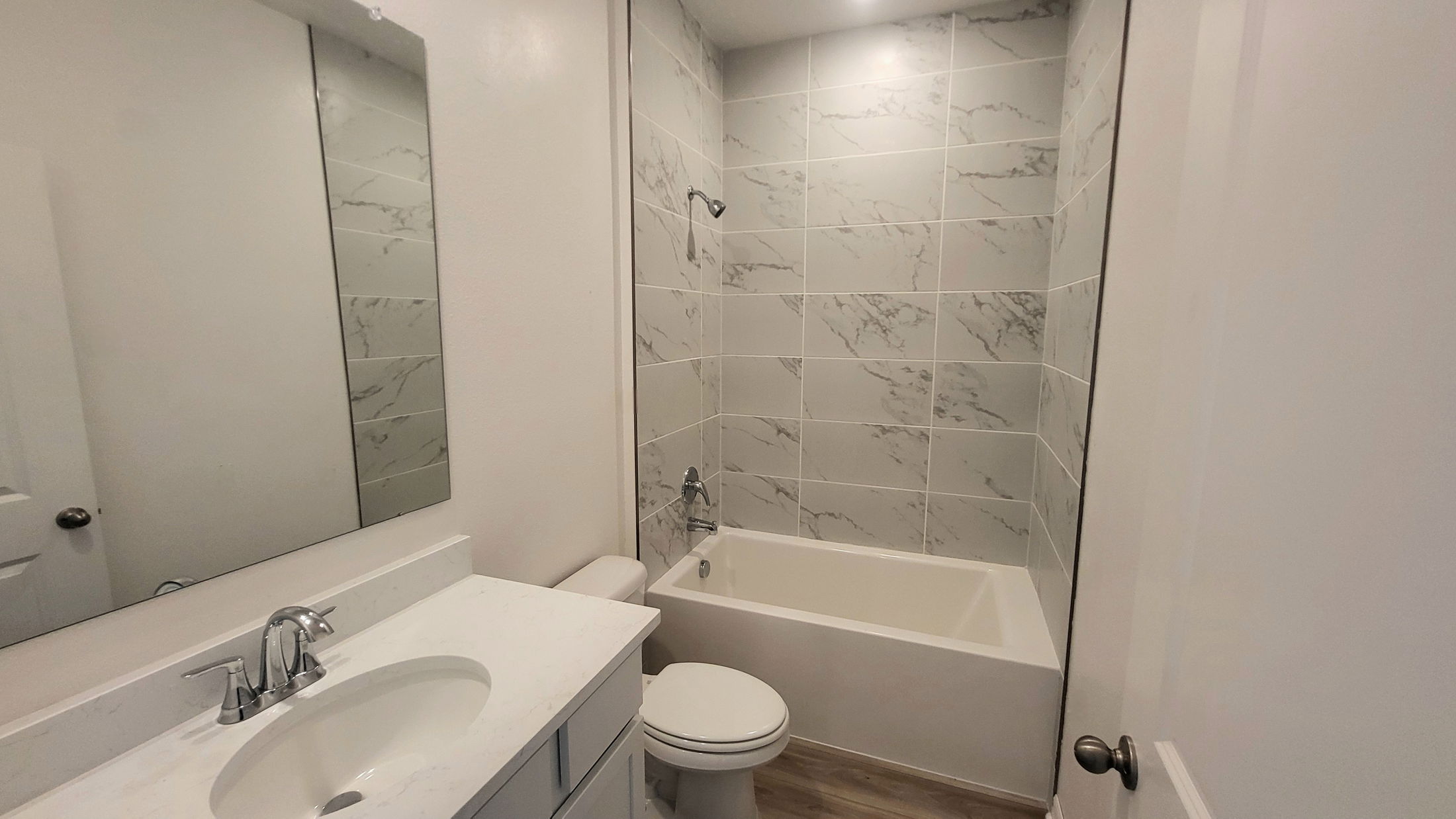 Modern bathroom with marble-tiled shower, white vanity, and wooden floor.