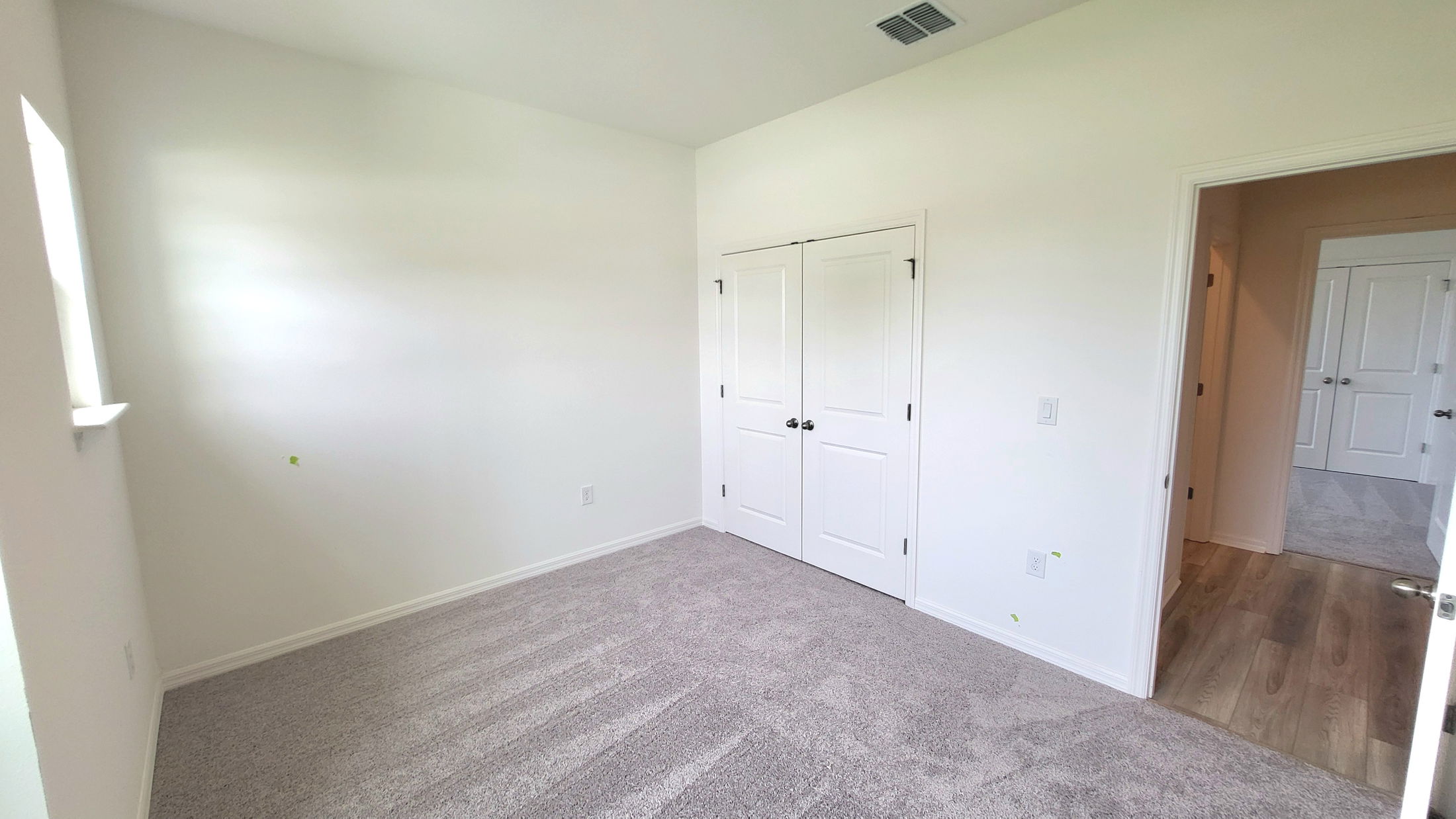 Empty white-walled room with carpet flooring and a double door closet.