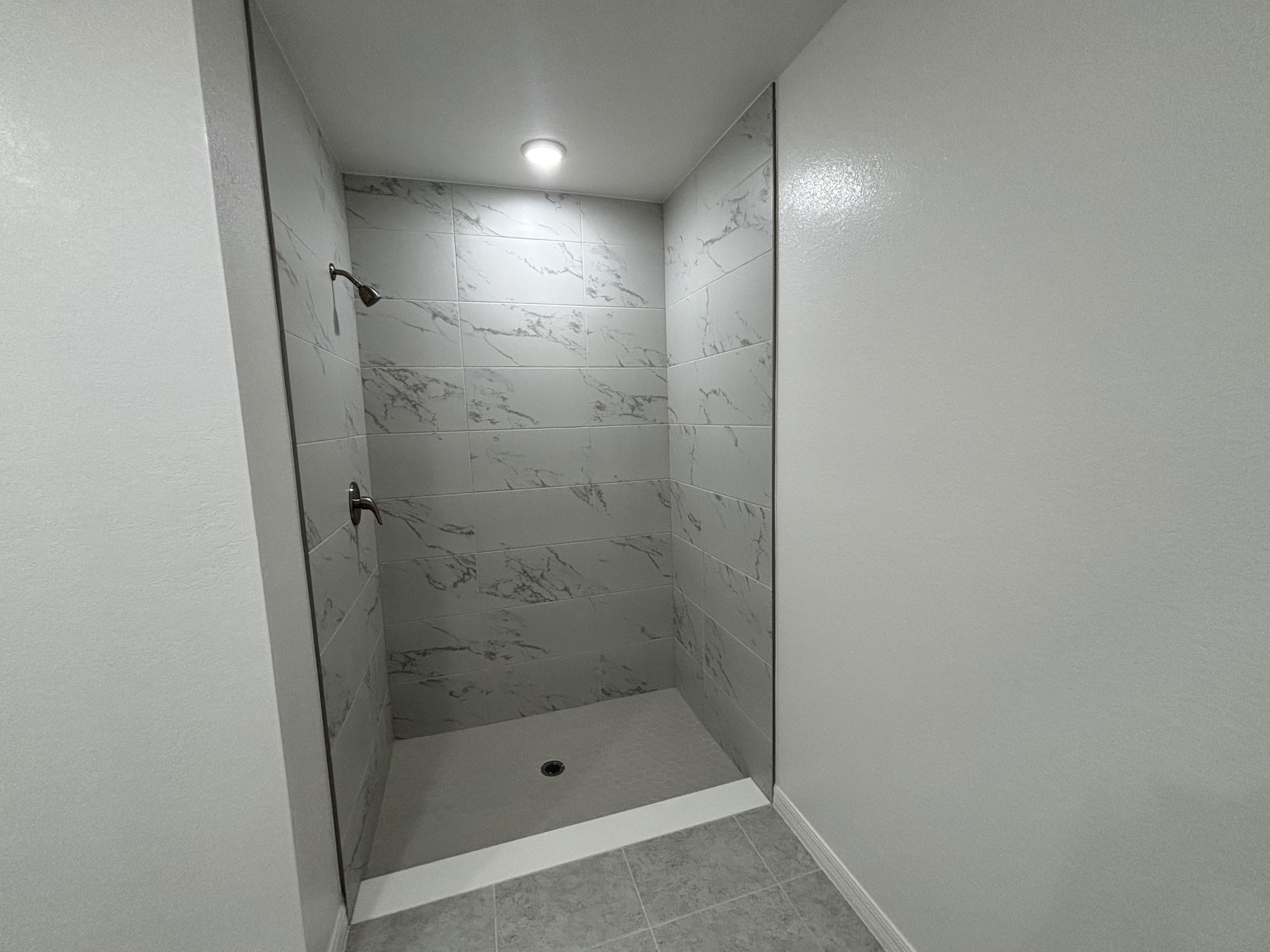 Modern shower design with gray marble tiles and sleek fixtures in a spacious bathroom.