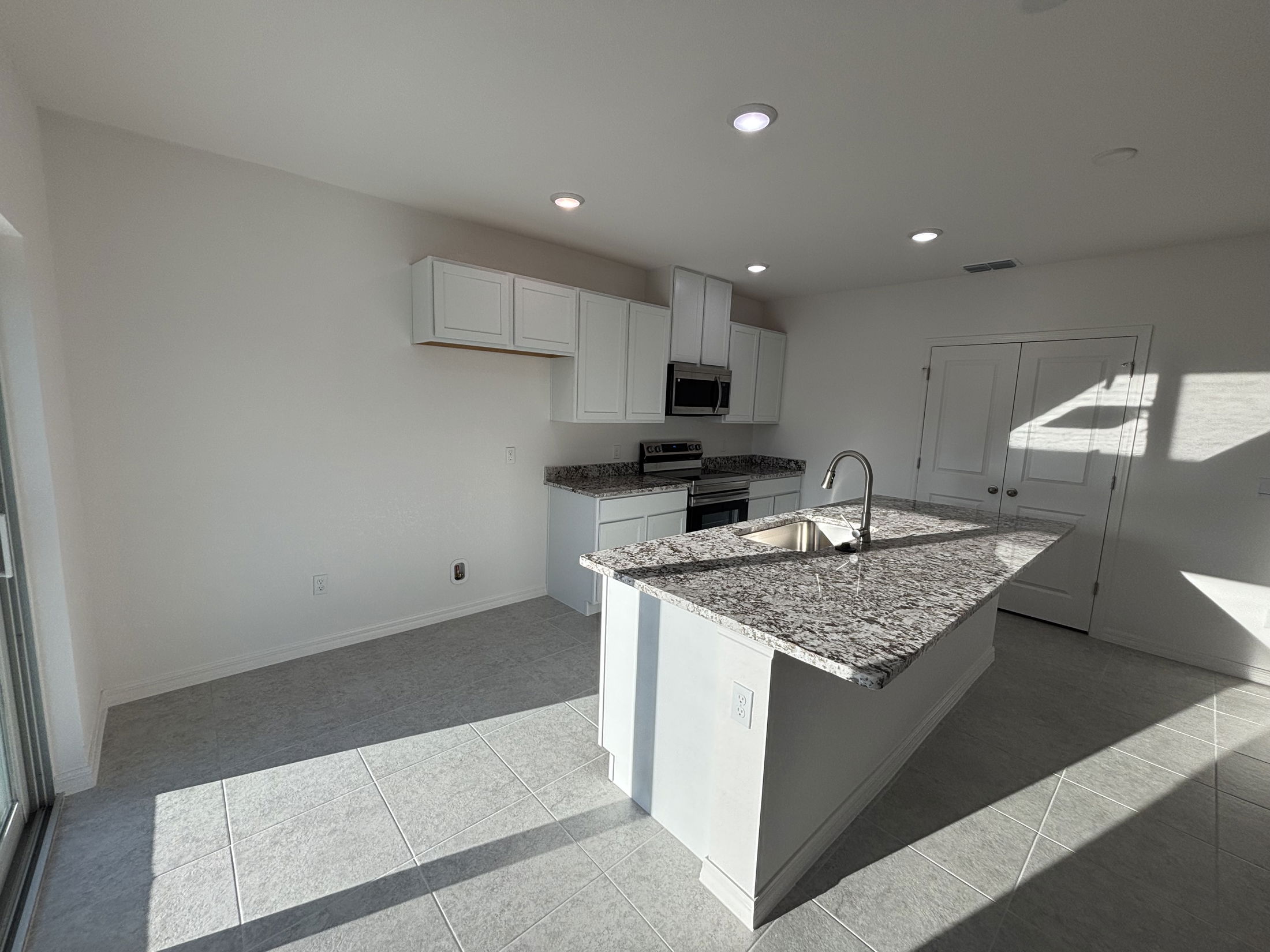 Modern kitchen interior featuring white cabinetry, granite countertops, and stainless steel appliances with ample natural light.