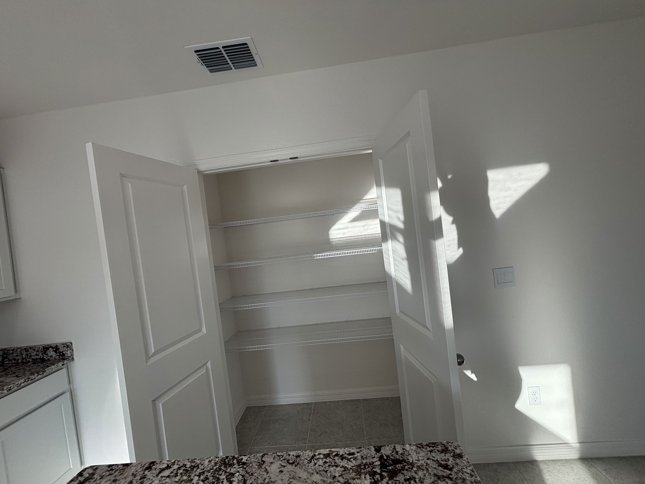 Interior view of a modern kitchen pantry with white shelves and sunlight casting shadows on the walls.