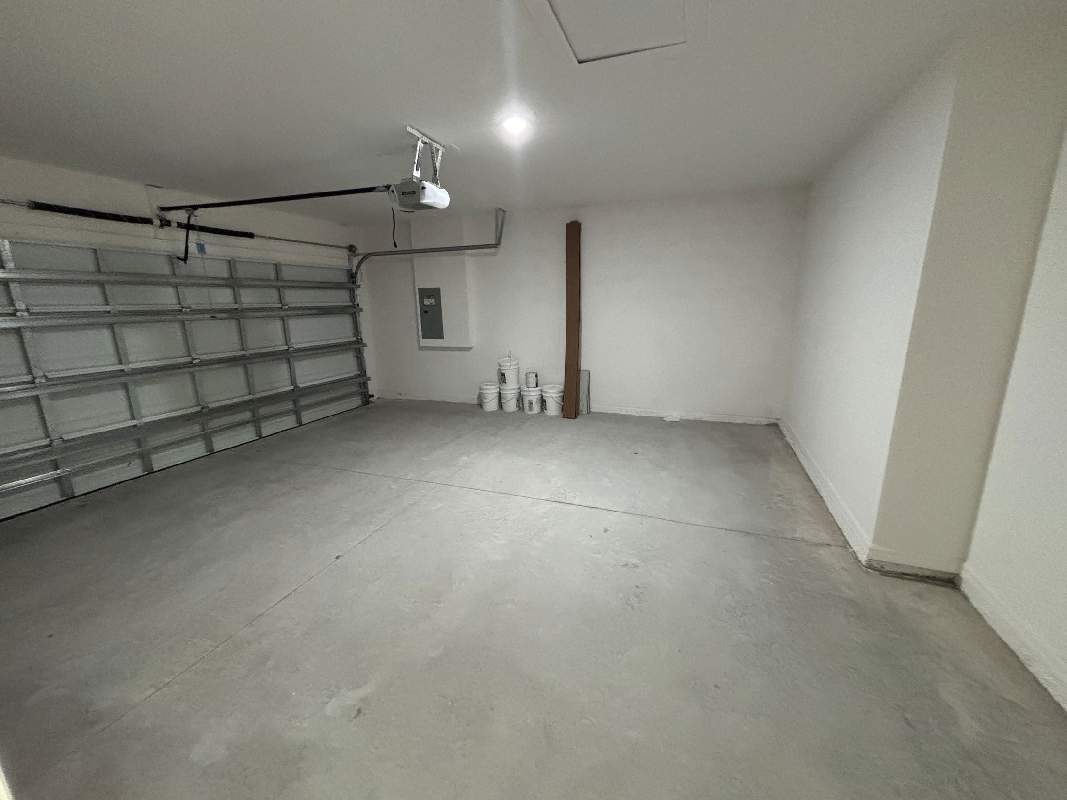 Spacious and empty garage interior with a garage door opener, electrical panel, and clean concrete flooring.