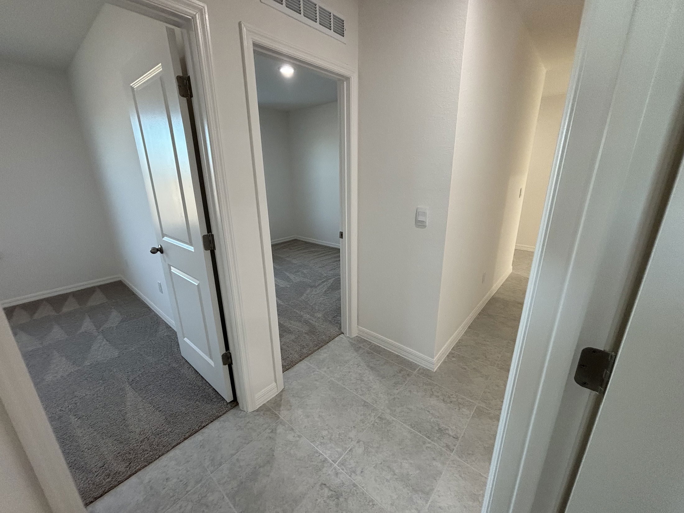 Interior view of a modern home hallway featuring two doors leading to adjacent rooms with neutral colors and carpeting.