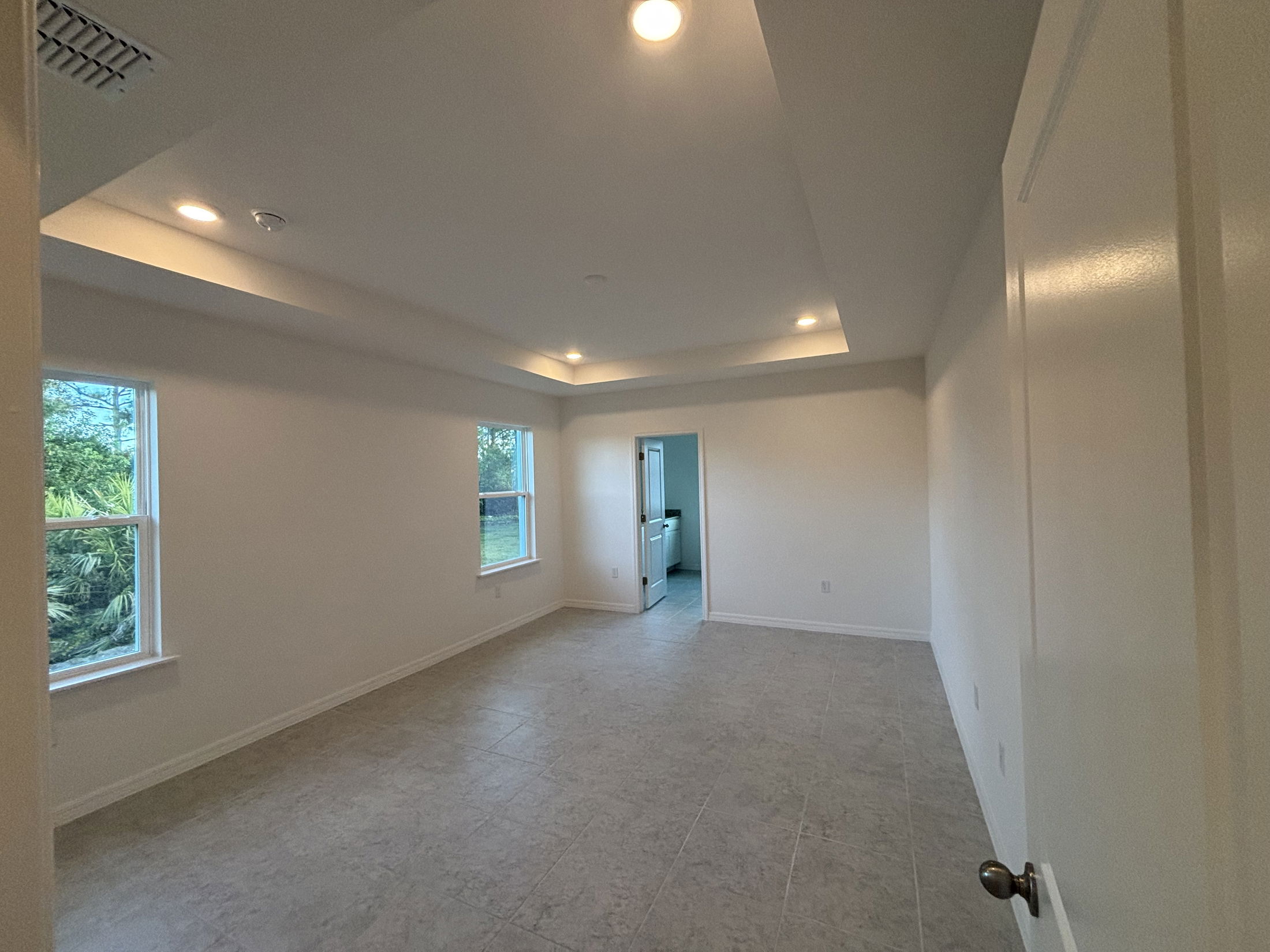 Spacious modern living room with tile flooring, recessed lighting, and large windows offering natural light and garden views.
