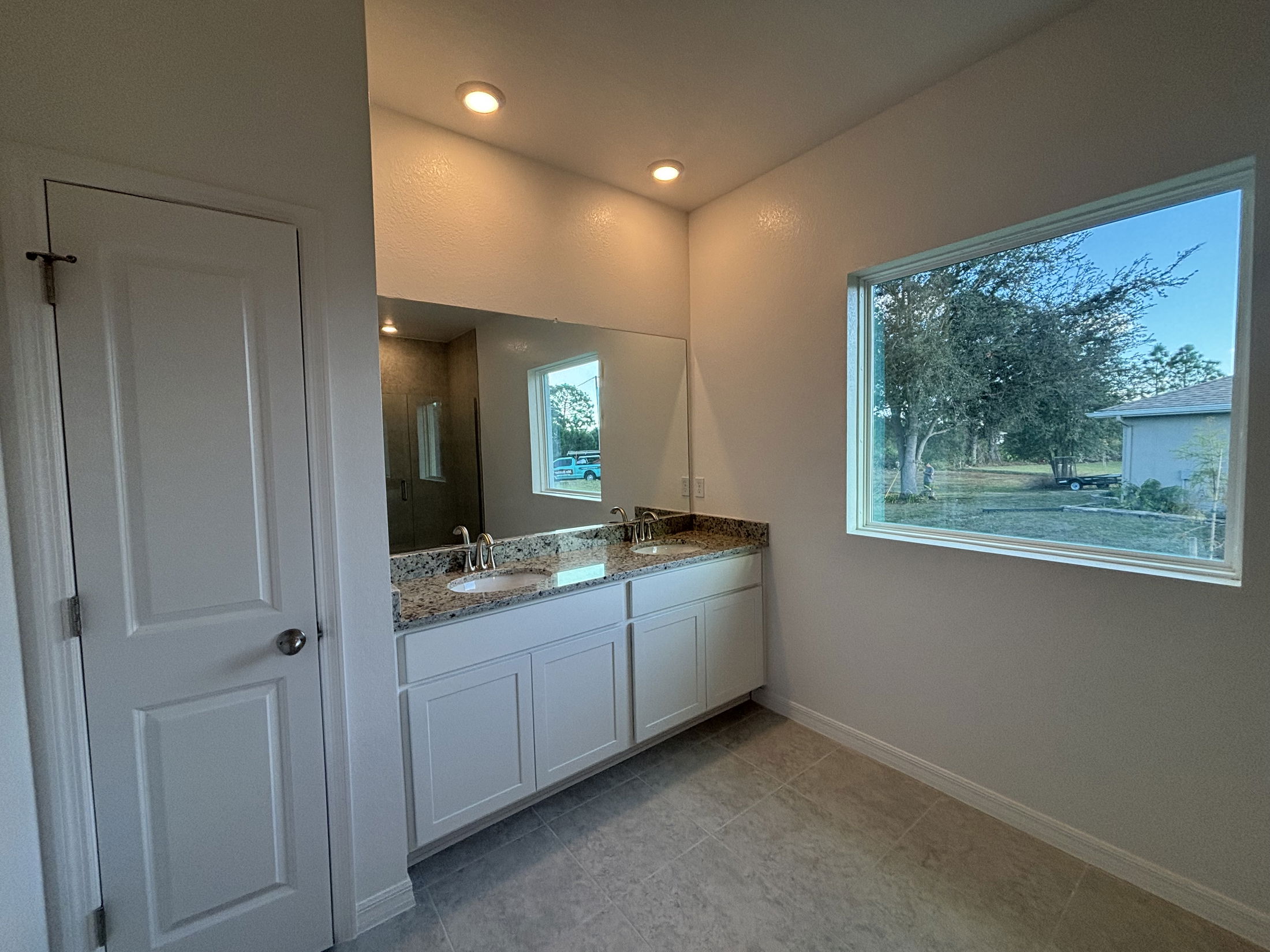 Spacious modern bathroom featuring granite countertops, a large mirror, and a window with outdoor views.