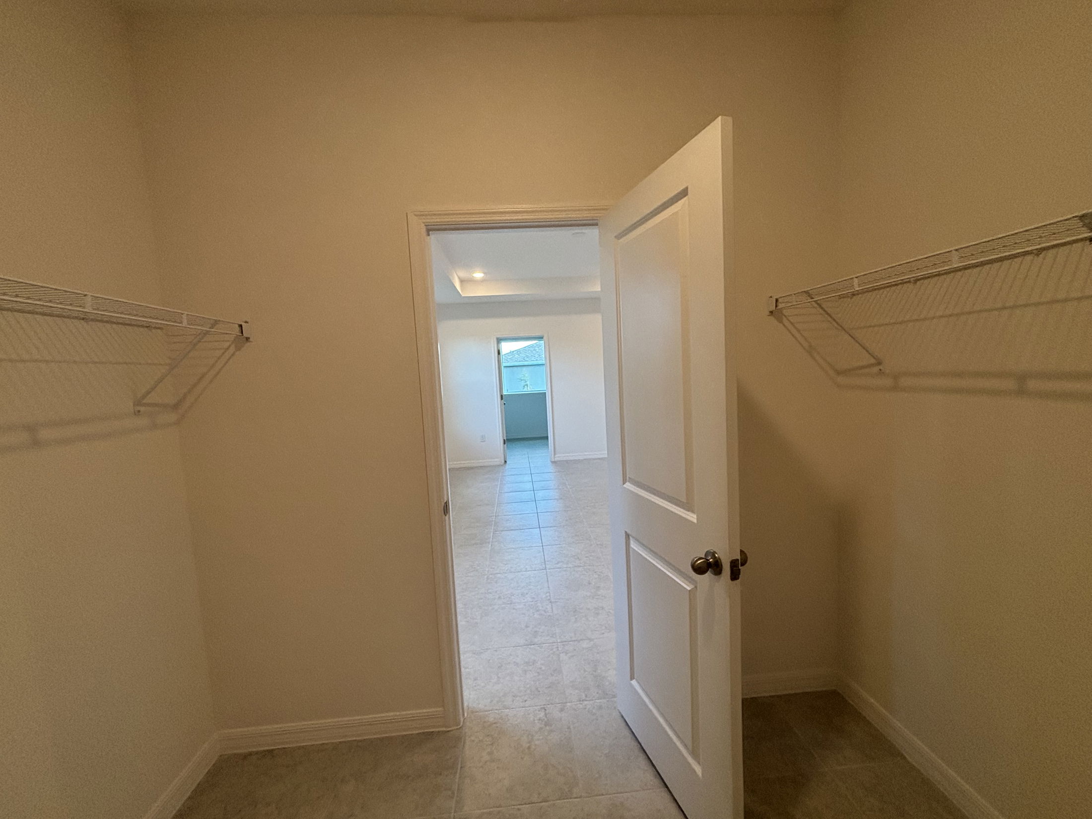 A spacious closet with wire shelving leads to a well-lit room with tiled flooring.